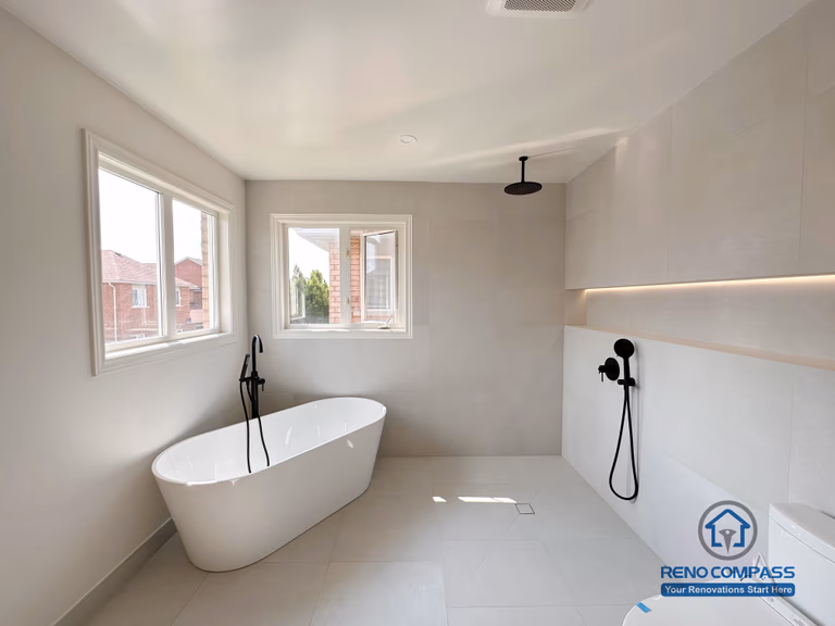 Modern bathroom renovation in Markham featuring a freestanding bathtub, walk-in shower, and wall-mounted matte black fixtures. Large-format tiles, soft natural light, and a minimalist layout create a calm, spa-like bathroom designed for comfort and everyday use.