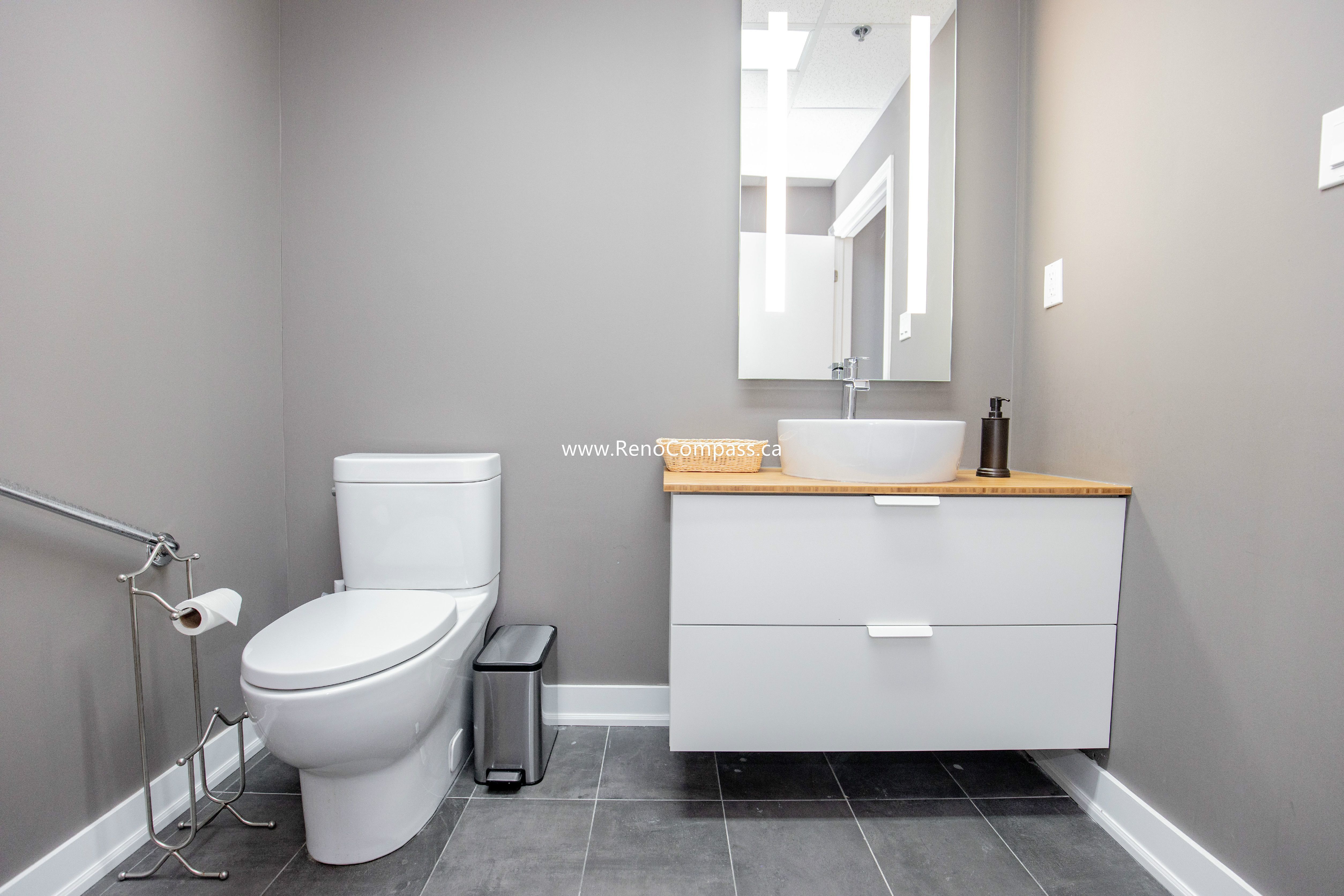 A professional commercial bathroom renovation featuring a modern floating vanity with a vessel sink, grey porcelain tile flooring, and ADA-compliant grab bars. Designed for comfort and style at The Singing School in Richmond Hill.