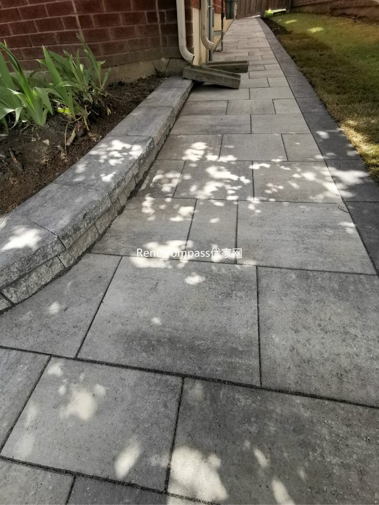 Beautifully finished side walkway interlocking project in Richmond Hill. The light gray stone pavers are neatly aligned against the house, featuring a raised garden border for a clean and modern look. Installed by RenoCompass for improved drainage, durability, and curb appeal.
