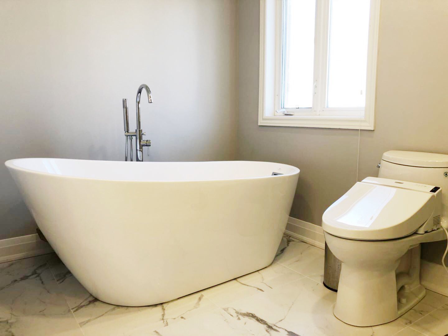 This Richmond Hill bathroom renovation features a modern freestanding soaking tub paired with marble-style flooring and a sleek floor-mounted faucet. The upgraded layout creates a spa-inspired atmosphere while maximizing comfort and visual space. A contemporary smart toilet and neutral color palette enhance both functionality and elegance. Completed by an experienced Toronto renovation company, this bathroom transformation combines luxury design, durable materials, and everyday convenience for a refined modern home.