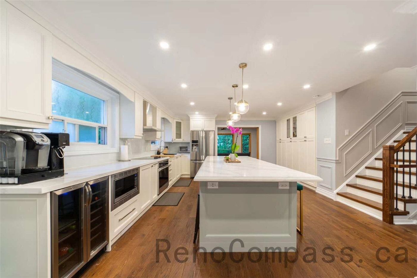 This open-concept kitchen is part of a North York interior renovation, featuring a spacious central island, custom white cabinetry, and warm hardwood flooring. Recessed ceiling lights and modern pendant fixtures enhance brightness and visual balance, while large windows provide natural daylight throughout the space. The layout improves workflow, storage, and family interaction, showcasing a practical yet elegant kitchen renovation solution commonly seen in high-quality Toronto interior renovation projects.