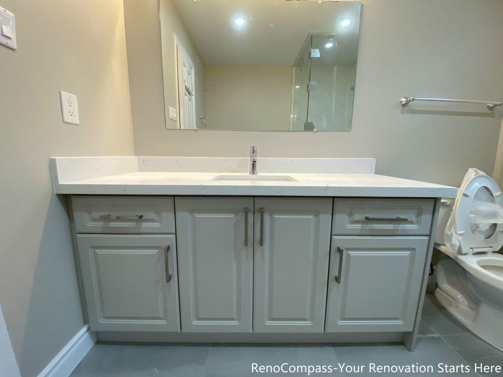This Mississauga interior renovation features a clean and functional bathroom vanity with a quartz countertop and integrated storage cabinets. The soft gray cabinetry is paired with sleek hardware and a wide mirror, creating a bright and organized vanity area suitable for daily use. The streamlined design improves storage efficiency while maintaining a modern, timeless look that complements the overall interior renovation.