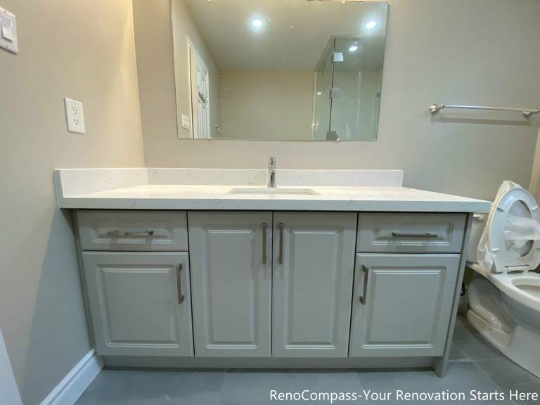 This Mississauga interior renovation features a clean and functional bathroom vanity with a quartz countertop and integrated storage cabinets. The soft gray cabinetry is paired with sleek hardware and a wide mirror, creating a bright and organized vanity area suitable for daily use. The streamlined design improves storage efficiency while maintaining a modern, timeless look that complements the overall interior renovation.
