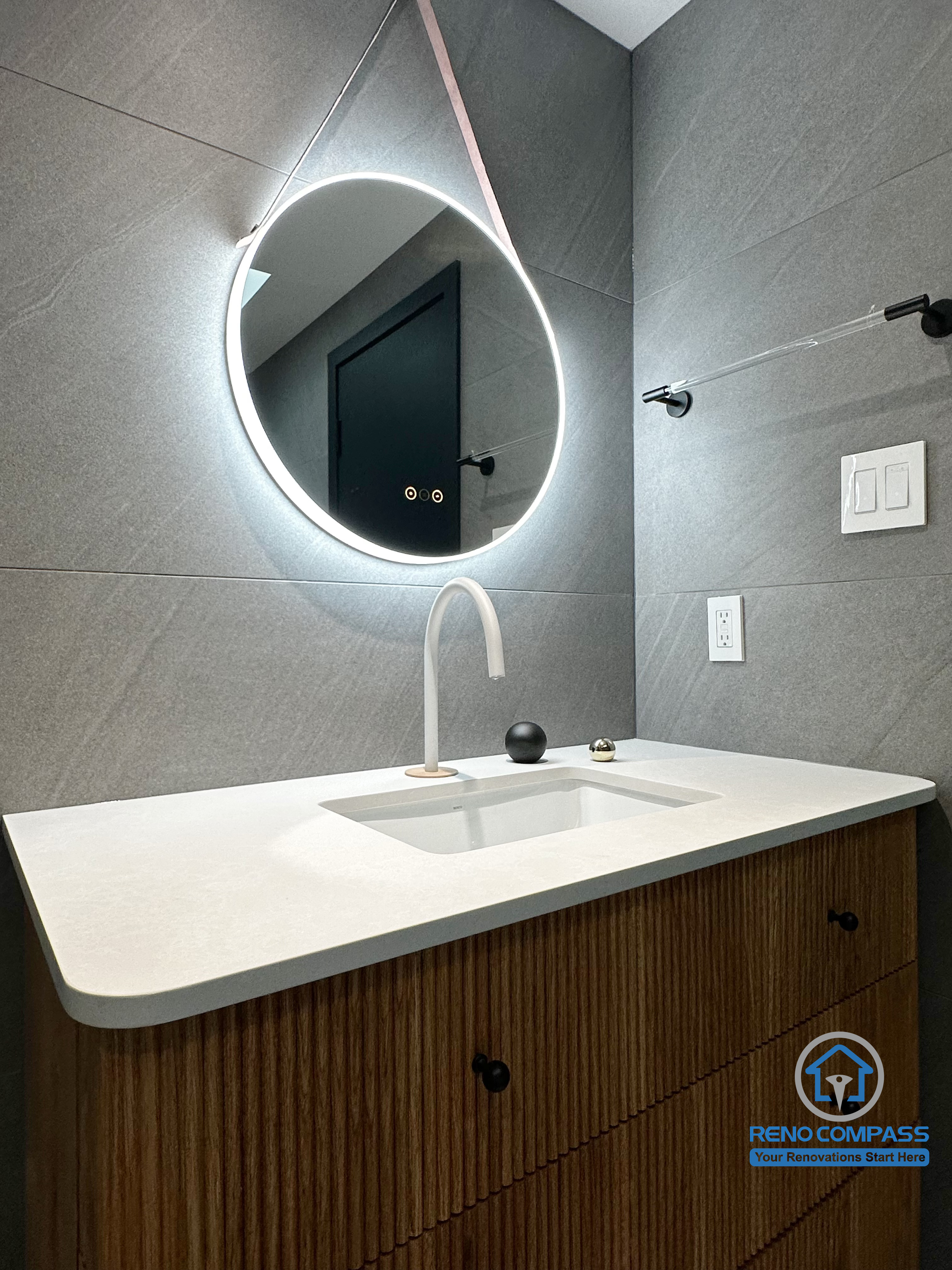 This detail shot highlights the bathroom vanity and backlit mirror from a Richmond Hill renovation. The integrated sink, sculptural modern faucet, and soft LED lighting create a clean, contemporary look, while the neutral grey tile backdrop enhances depth and visual balance. Designed and completed by Reno Compass, this space reflects a refined modern bathroom aesthetic within the Greater Toronto Area.