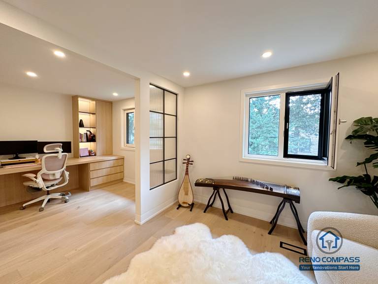This Toronto interior renovation showcases a combined home office and living area featuring light hardwood flooring, custom built-in cabinetry, and modern glass partition design. The open yet functional layout enhances natural light and workflow while maintaining visual separation, highlighting high-quality craftsmanship ideal for contemporary Toronto home renovations.