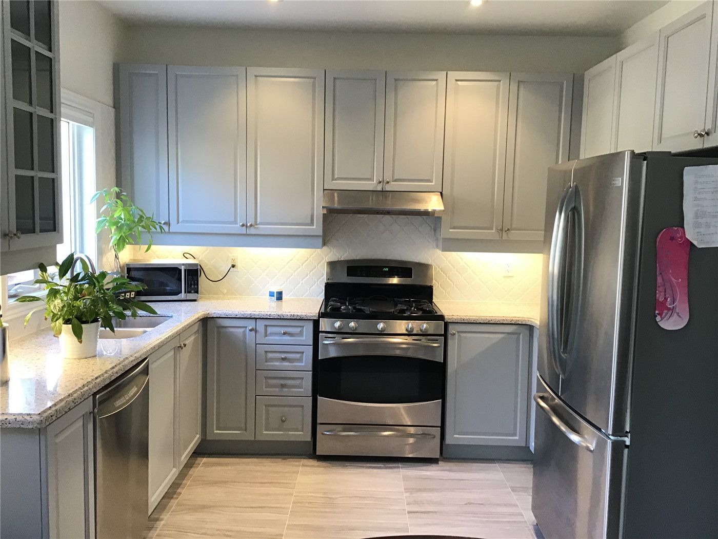 This Woodbridge interior renovation features a clean and modern kitchen design with grey shaker cabinets, quartz countertops, and stainless steel appliances. The layout maximizes functionality with an L-shaped counter, built-in dishwasher, and bright natural lighting, creating a practical yet stylish cooking space for everyday living.