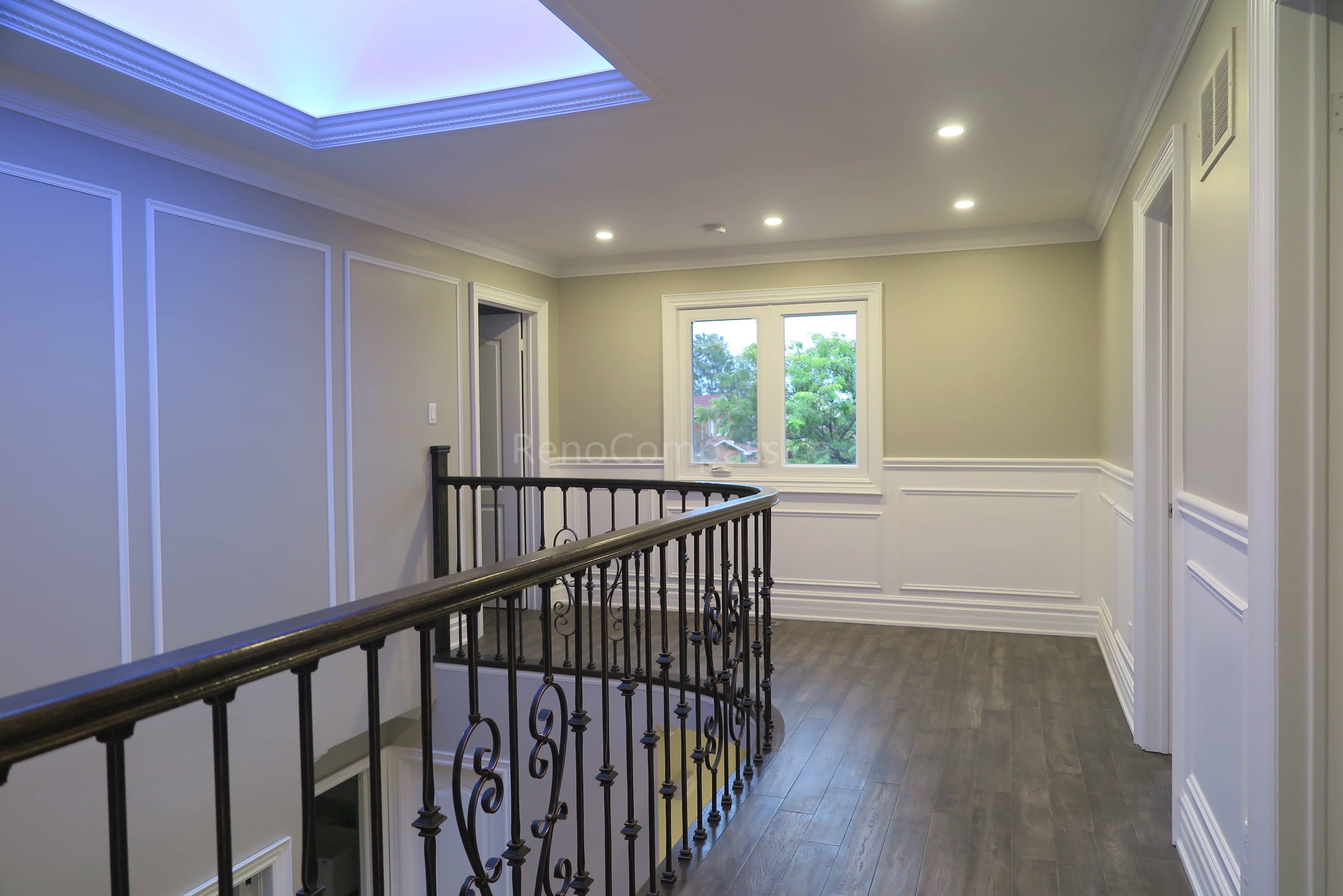 This Markham interior renovation showcases an elegant upper hallway and staircase area featuring custom wrought iron railings, detailed wall panel molding, and modern hardwood flooring. The space is enhanced by recessed lighting and a contemporary tray ceiling with soft ambient illumination, creating a bright and refined transition between levels. Completed by Reno Compass, a trusted renovation contractor specializing in custom interior finishing and full home renovations across Markham and the Greater Toronto Area.