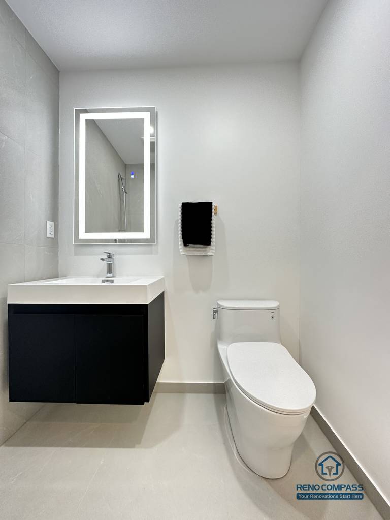 This image features a clean and modern accessible bathroom layout in Brampton, highlighting a floating vanity, integrated LED mirror, and a compact toilet designed for efficient space use. The wall-mounted vanity improves floor clearance, making the bathroom easier to clean and more accessible for daily use and pet care. Neutral-toned tiles and minimal fixtures create a calm, functional environment suitable for barrier-free living. This thoughtfully planned bathroom renovation was completed by an experienced Toronto Renovation Company specializing in accessible and pet-friendly home solutions.