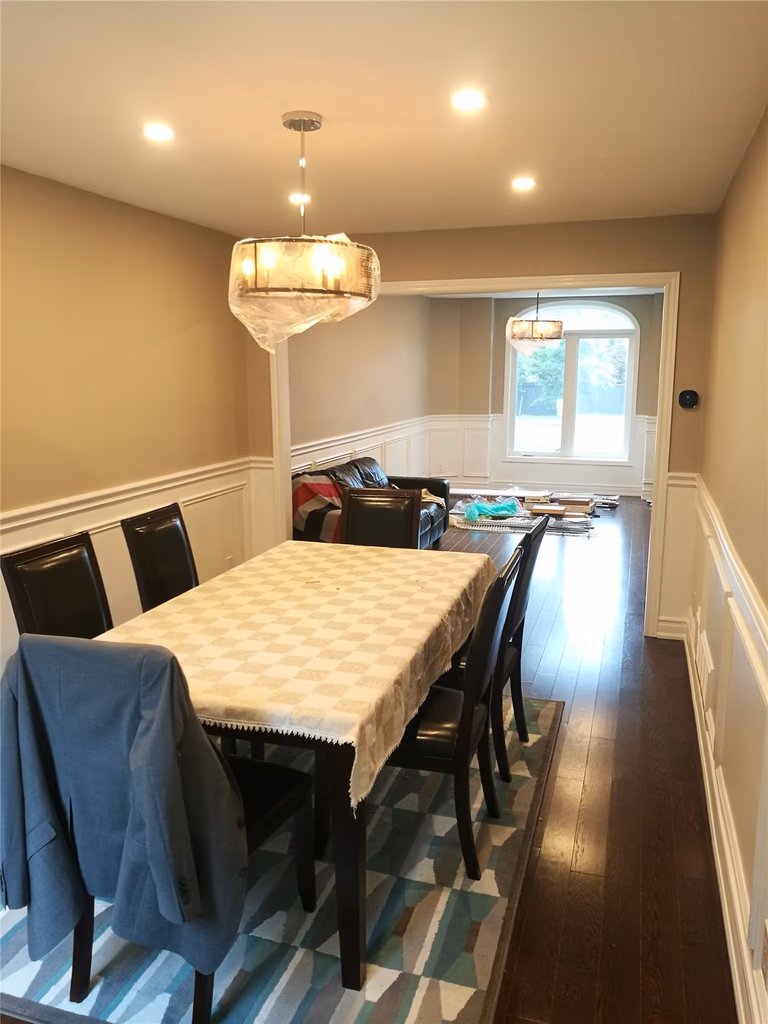 This Newmarket interior renovation features an upgraded dining area with dark hardwood flooring, elegant wall paneling, and a modern pendant light combined with recessed ceiling lights. The refreshed layout enhances both lighting quality and spatial flow, showcasing the craftsmanship and attention to detail of a professional Toronto renovation company.