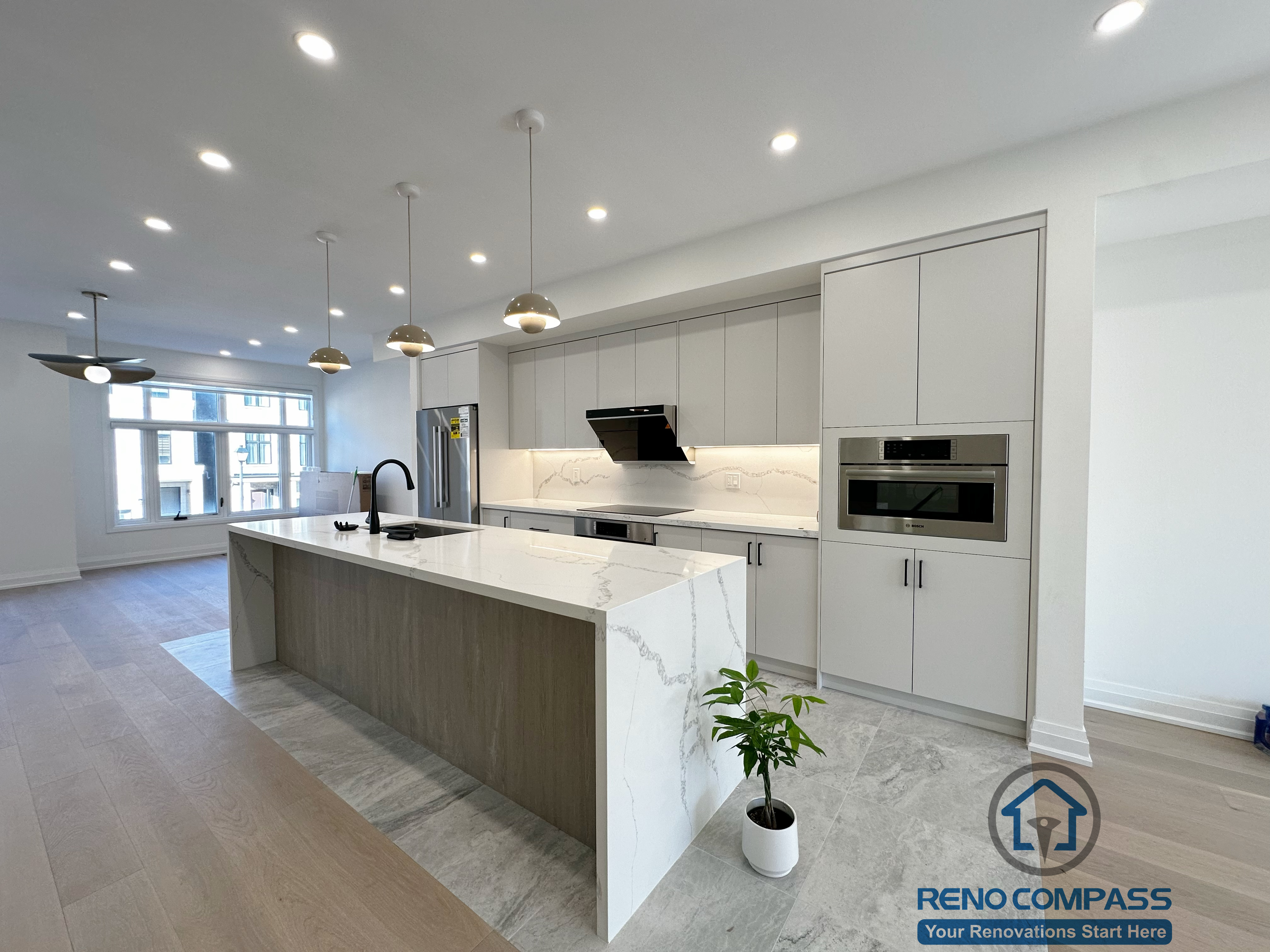 This image highlights the open-concept kitchen design in this Richmond Hill interior renovation, featuring a large quartz waterfall island with integrated storage and seating. Floor-to-ceiling custom cabinetry, built-in appliances, and continuous recessed lighting enhance the clean architectural lines, while pendant lights and warm flooring create a balanced, livable atmosphere.