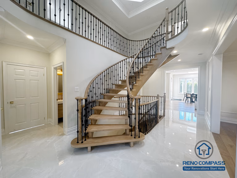 This image showcases the front view of a grand curved staircase as part of a North York flooring and stair renovation. The staircase features solid hardwood treads, smooth curved stringers, and decorative iron balusters, forming a strong architectural focal point at the home’s entrance. The surrounding flooring is finished with polished, light-toned surfaces that enhance brightness and reflect natural light. This renovation highlights precise craftsmanship and seamless coordination between flooring and stair design, creating an elegant and cohesive interior for North York homes.