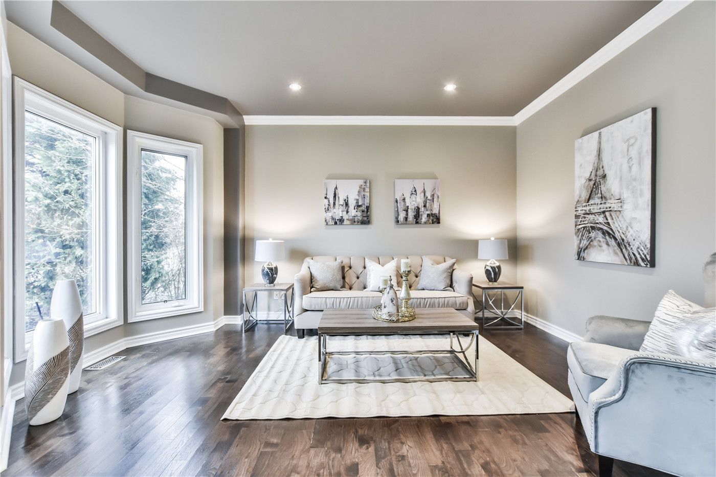 This Toronto interior design pre-sale staging highlights a stylish family living room with modern lighting, neutral-tone sofa, accent chair, and layered décor. The soft area rug, contemporary artwork, and coordinated furniture layout create a cozy yet upscale atmosphere that enhances space and comfort.