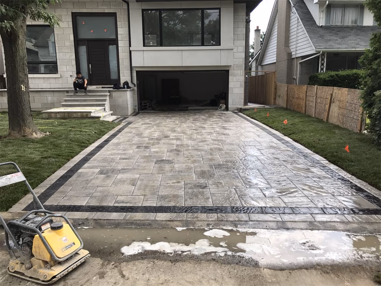 Front yard landscaping renovation in Toronto featuring a large interlocking driveway with decorative stone borders and clean modern paving patterns. The project improves curb appeal while providing a durable and functional driveway surface for everyday use.