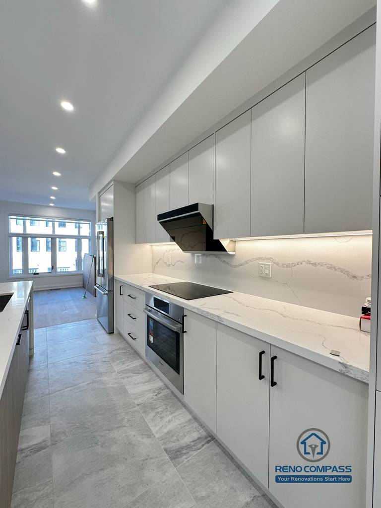 This Richmond Hill kitchen features flat-panel cabinetry, quartz countertops with subtle veining, integrated range hood, and continuous under-cabinet lighting, delivering a streamlined and functional cooking workspace.