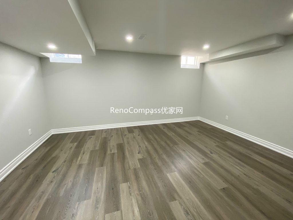 Modern basement renovation in Richmond Hill featuring open layout design, high-quality wooden floors, and elegant white baseboards. Reno Compass transformed this space into a bright and functional lower level.