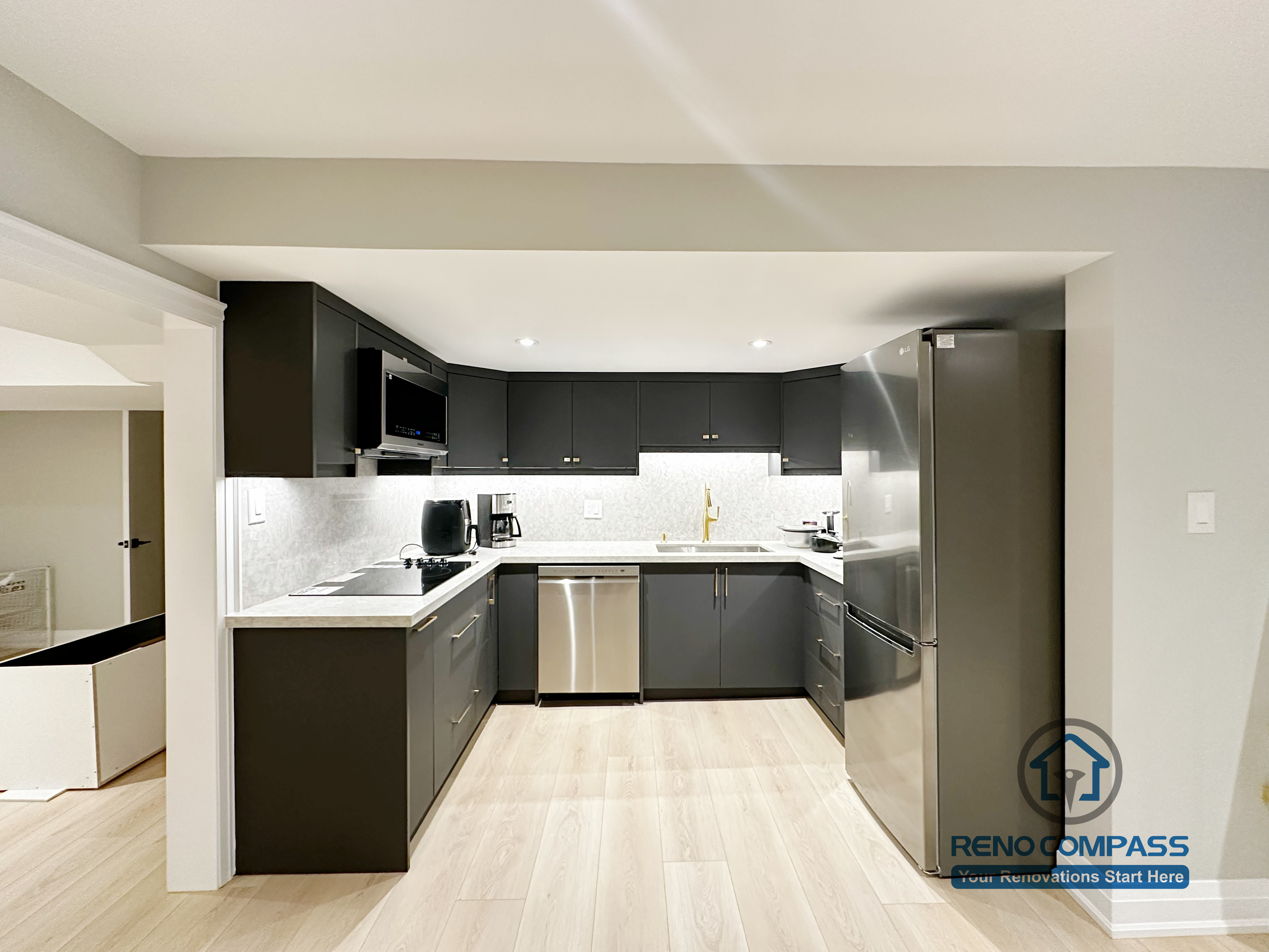 Basement renovation in Richmond Hill featuring a modern kitchenette with matte black cabinetry, stainless steel appliances, quartz-style countertops, and efficient space planning for daily use.