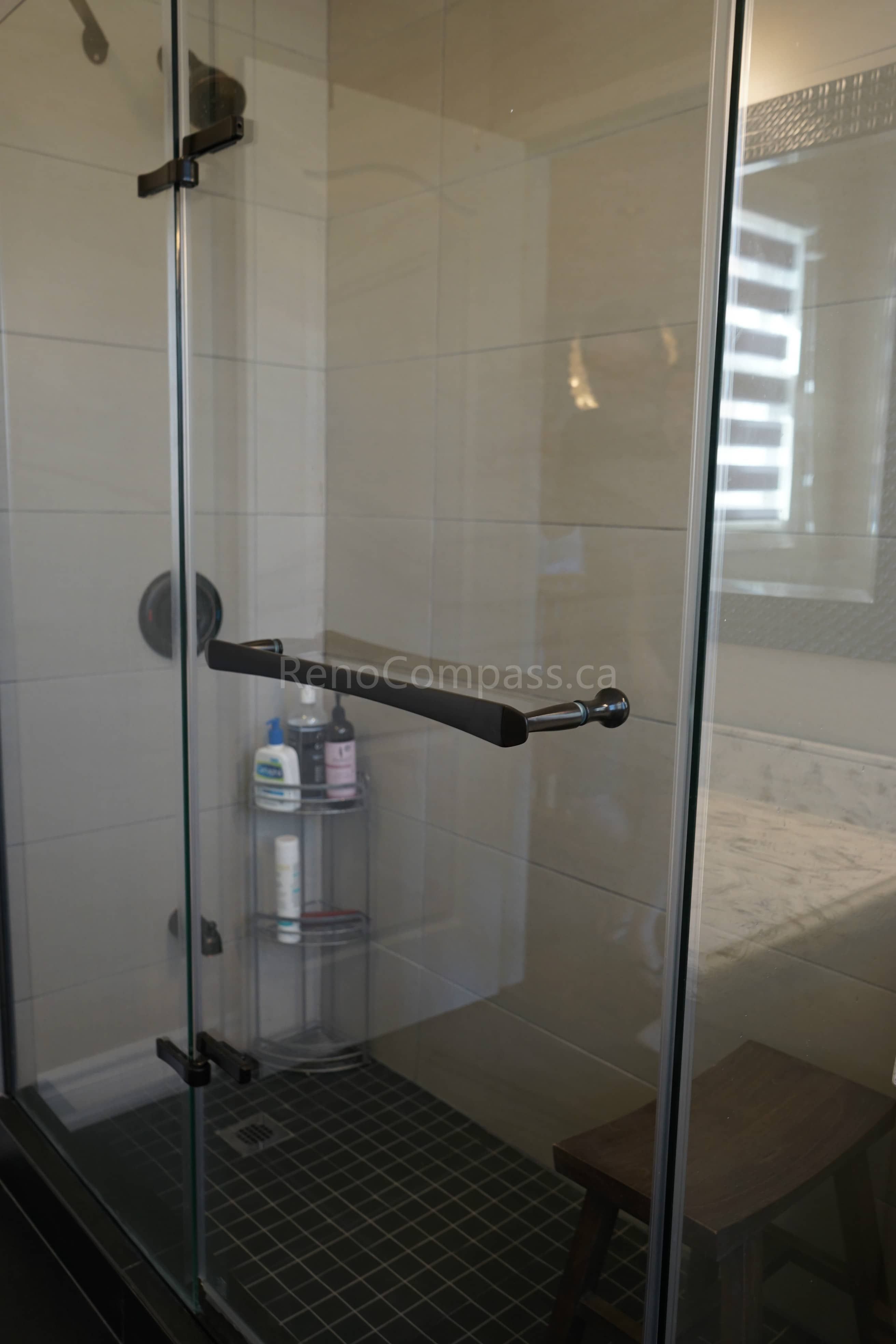 This bathroom renovation features a modern glass walk-in shower enclosure with sleek matte black hardware and tiled shower walls. The frameless glass design enhances natural light and creates an open, spacious feel, while the upgraded fixtures and flooring provide both durability and contemporary style.