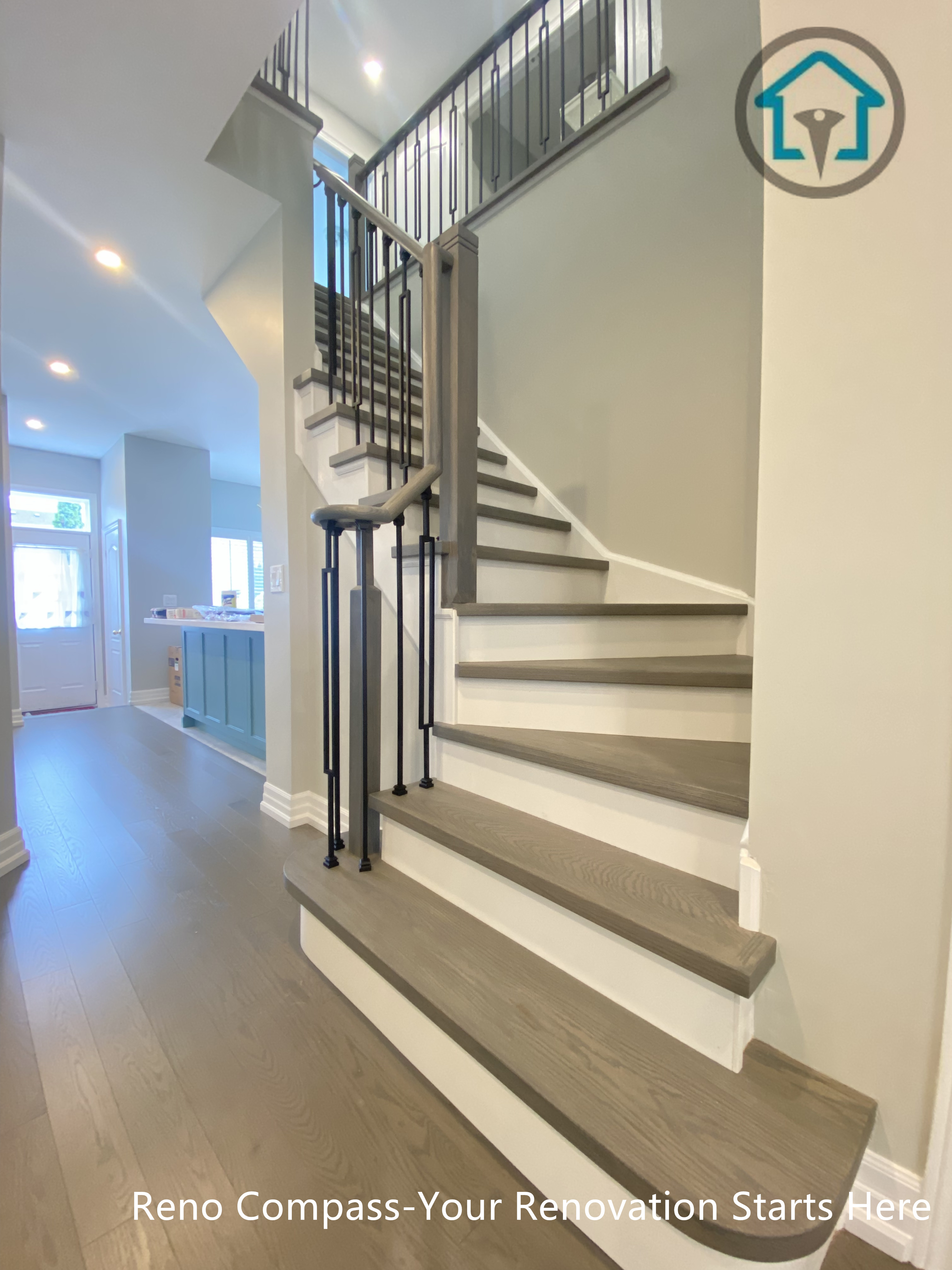 This modern staircase renovation features warm wood treads paired with crisp white risers and slim black metal railings, creating a clean and open visual transition between floors. The design improves circulation, sightlines, and natural light flow while maintaining safety and structural clarity. Carefully coordinated finishes allow the staircase to integrate seamlessly with the surrounding flooring and kitchen area, delivering a cohesive interior renovation by Reno Compass.