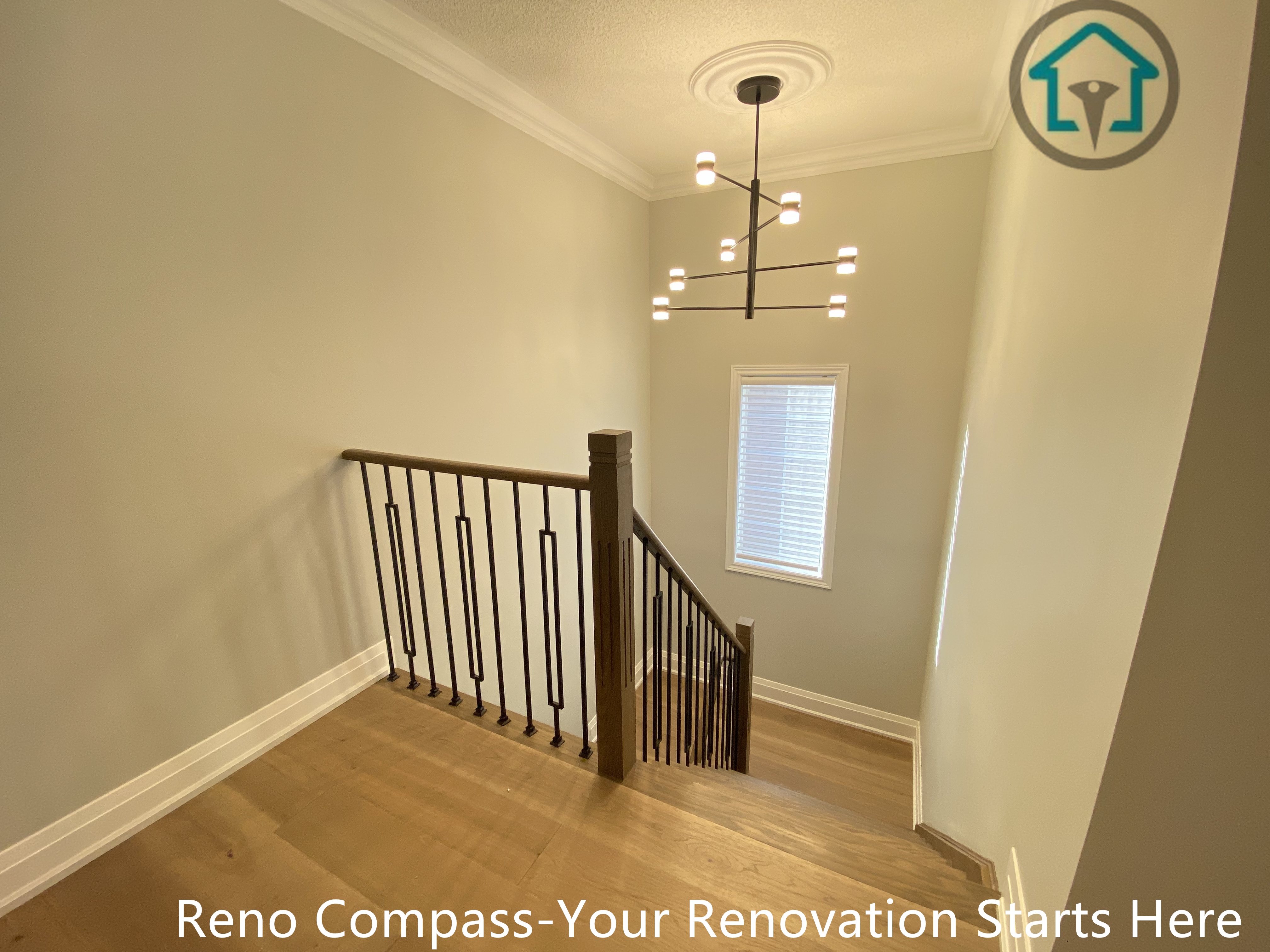 This image highlights the staircase landing area of a flooring and stair renovation project in Richmond Hill. The space features seamless hardwood flooring, clean white walls, and modern black iron railings that enhance safety while maintaining an open, airy feel. Natural light from the window and a contemporary chandelier add visual height and elegance to the stairwell. Completed by a professional Toronto renovation company, this renovation focuses on smooth transitions between levels, durable materials, and a refined modern aesthetic suitable for long-term residential living.