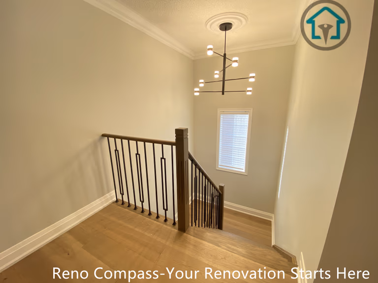 This image highlights the staircase landing area of a flooring and stair renovation project in Richmond Hill. The space features seamless hardwood flooring, clean white walls, and modern black iron railings that enhance safety while maintaining an open, airy feel. Natural light from the window and a contemporary chandelier add visual height and elegance to the stairwell. Completed by a professional Toronto renovation company, this renovation focuses on smooth transitions between levels, durable materials, and a refined modern aesthetic suitable for long-term residential living.
