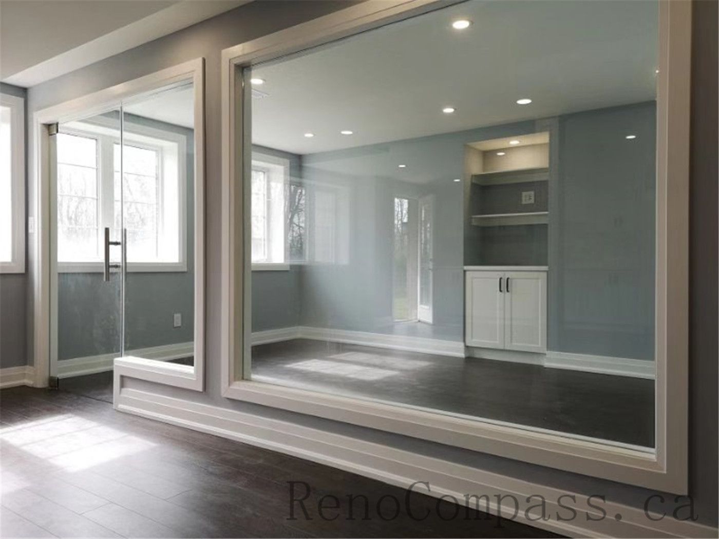 This contemporary basement renovation in Aurora features floor-to-ceiling mirrors, a sleek glass partition, recessed lighting, and built-in storage cabinetry. The design enhances natural light and creates an open, spacious atmosphere — expertly completed by RenoCompass.