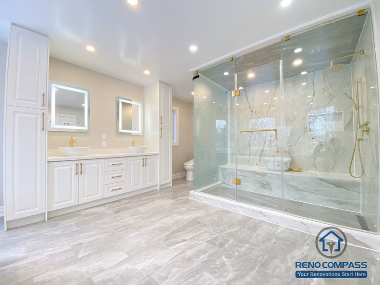 This Richmond Hill bathroom renovation showcases a bright and elegant design featuring a frameless glass shower enclosure, built-in bathtub, marble-style wall tiles, and gold-finish fixtures. The custom white vanity with integrated lighting mirror and large-format floor tiles enhance both functionality and visual openness. This project reflects high-quality craftsmanship and thoughtful layout planning for a modern bathroom renovation in Richmond Hill.