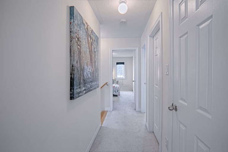 This modern hallway renovation features a clean neutral palette, soft carpeting, and bright overhead lighting that enhances the sense of openness throughout the upper floor. The streamlined layout connects bedrooms and living spaces seamlessly, while contemporary wall art adds visual interest and warmth. Designed to improve flow, comfort, and everyday functionality, this interior upgrade reflects the high-quality craftsmanship of a trusted Toronto renovation company specializing in full home renovation and modern residential interiors.