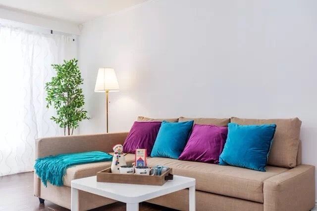 This Toronto interior renovation showcases a clean and modern living room transformation featuring neutral wall colors, comfortable sectional seating, and vibrant accent cushions. Large windows allow abundant natural light to enhance the bright and welcoming atmosphere. The design blends simplicity, comfort, and functionality, creating a stylish and relaxing living space for everyday living in a modern Toronto home.