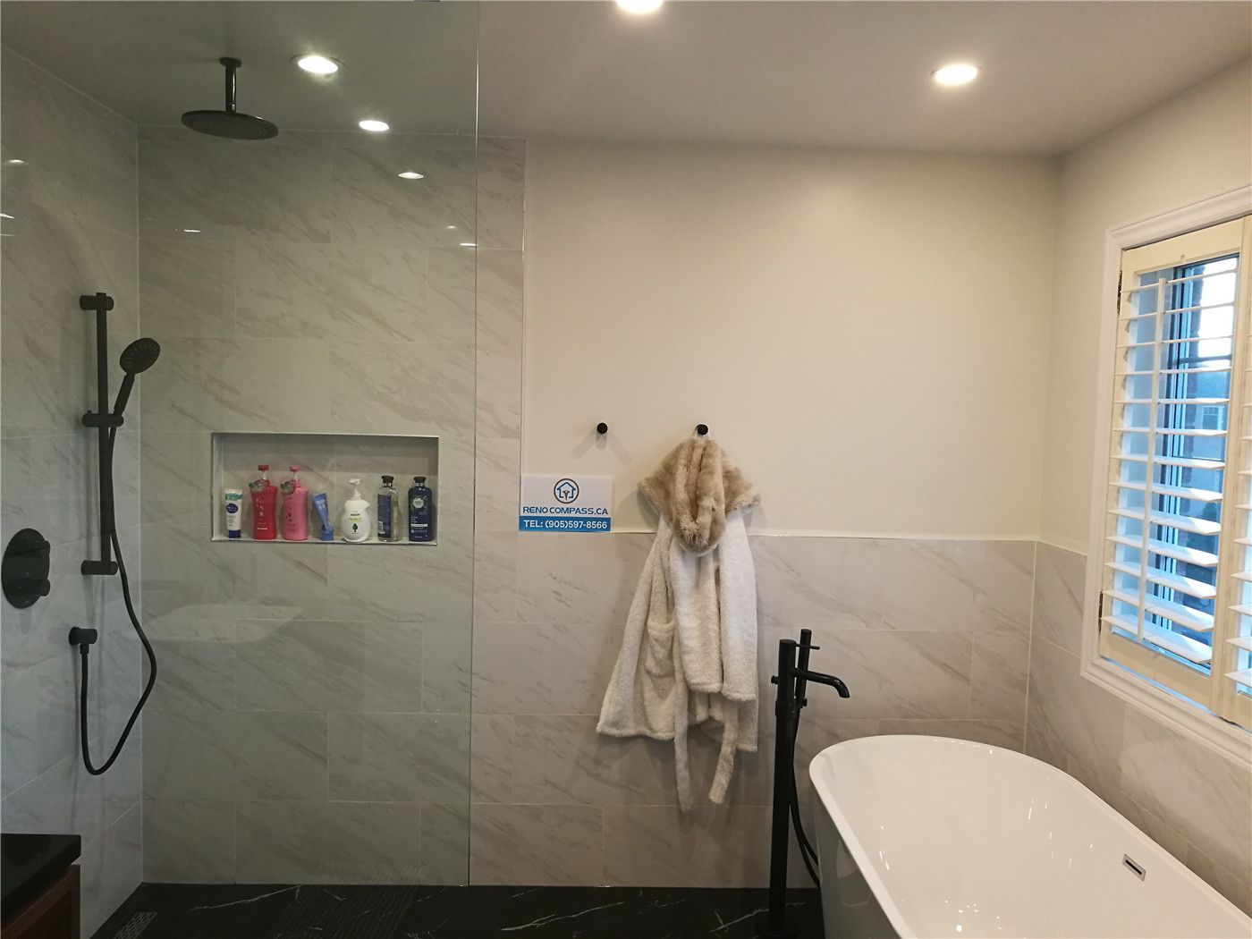 This Richmond Hill bathroom renovation features a modern luxury design with a spacious walk-in glass shower, built-in wall niche shelving, large-format marble-style tiles, and a freestanding soaking bathtub with matte black fixtures. Recessed lighting and clean wall finishes enhance brightness and comfort, creating a spa-like atmosphere for everyday living. Completed by a professional Toronto renovation company, this project showcases high-quality craftsmanship and contemporary bathroom renovation solutions for homeowners in Richmond Hill and across the GTA.