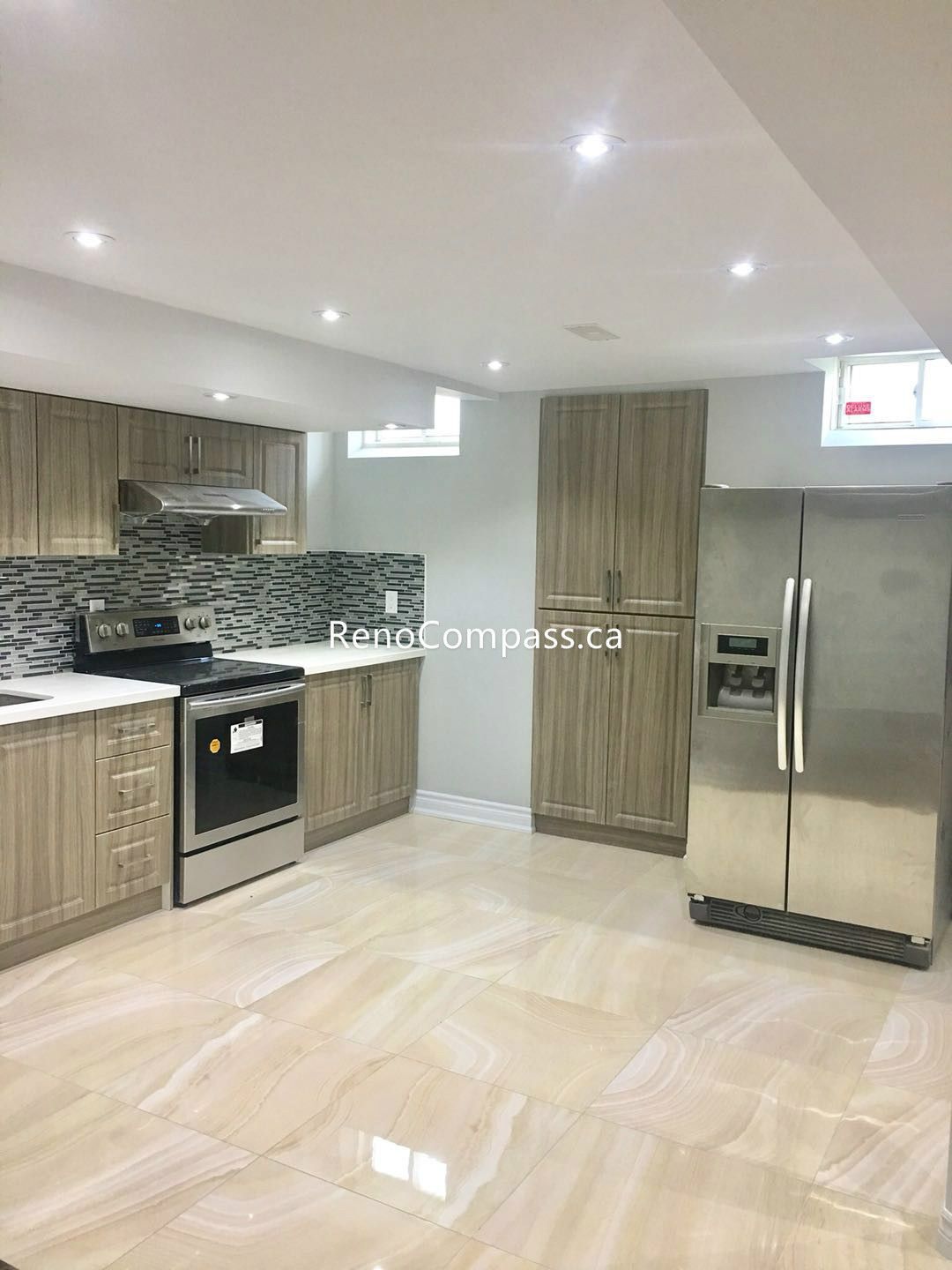 This Toronto basement renovation features a fully finished modern basement kitchen with custom wood-style cabinetry, quartz countertops, and a stylish mosaic backsplash. The space is equipped with stainless steel appliances, including a full-size refrigerator and built-in oven, creating a functional and contemporary cooking area. Bright lighting, durable tile flooring, and efficient layout design make this basement kitchen ideal for rental or family use. Completed by a professional Toronto renovation company, the project highlights quality craftsmanship and modern basement living solutions.