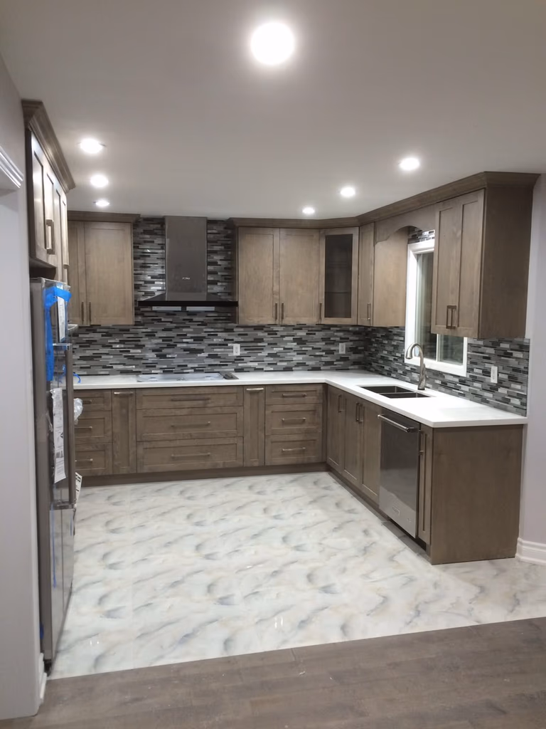 This Toronto interior renovation project features a complete kitchen upgrade with modern cabinetry, durable countertops, and a stylish mosaic tile backsplash. The space was redesigned to improve functionality and storage while maintaining a clean and contemporary look.

Custom wood-tone cabinets provide ample storage and a warm aesthetic, paired with bright countertops and a patterned backsplash that adds depth and visual interest. Recessed pot lights enhance overall lighting, creating a brighter and more inviting cooking environment. The updated flooring and efficient layout ensure easy maintenance and daily convenience for homeowners.

Completed by a professional Toronto renovation company, this kitchen renovation highlights quality craftsmanship, practical design solutions, and a balanced combination of modern style and everyday functionality.