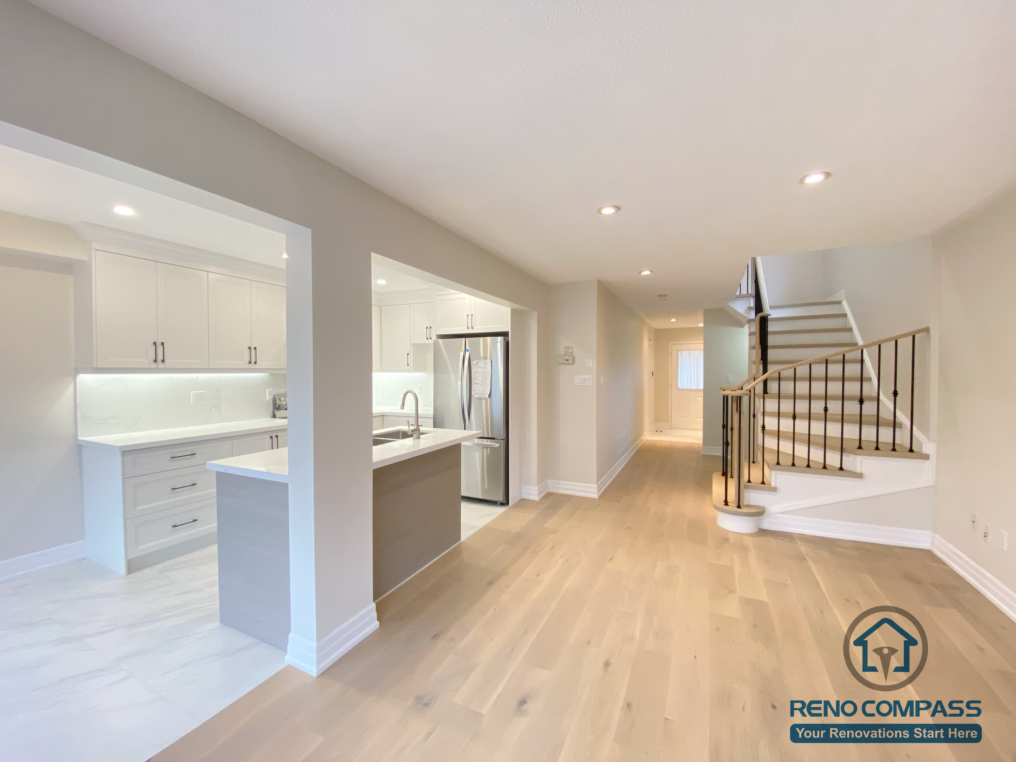 This Markham interior renovation showcases an open-concept layout that seamlessly connects the kitchen, living area, and staircase. The space features wide-plank hardwood flooring, a modern kitchen with white cabinetry and quartz countertops, and a refined staircase with hardwood treads and black metal railings. Recessed lighting enhances brightness and continuity throughout the main floor. Completed by a professional Toronto renovation company, this design improves circulation, visual balance, and everyday functionality for a Markham home.