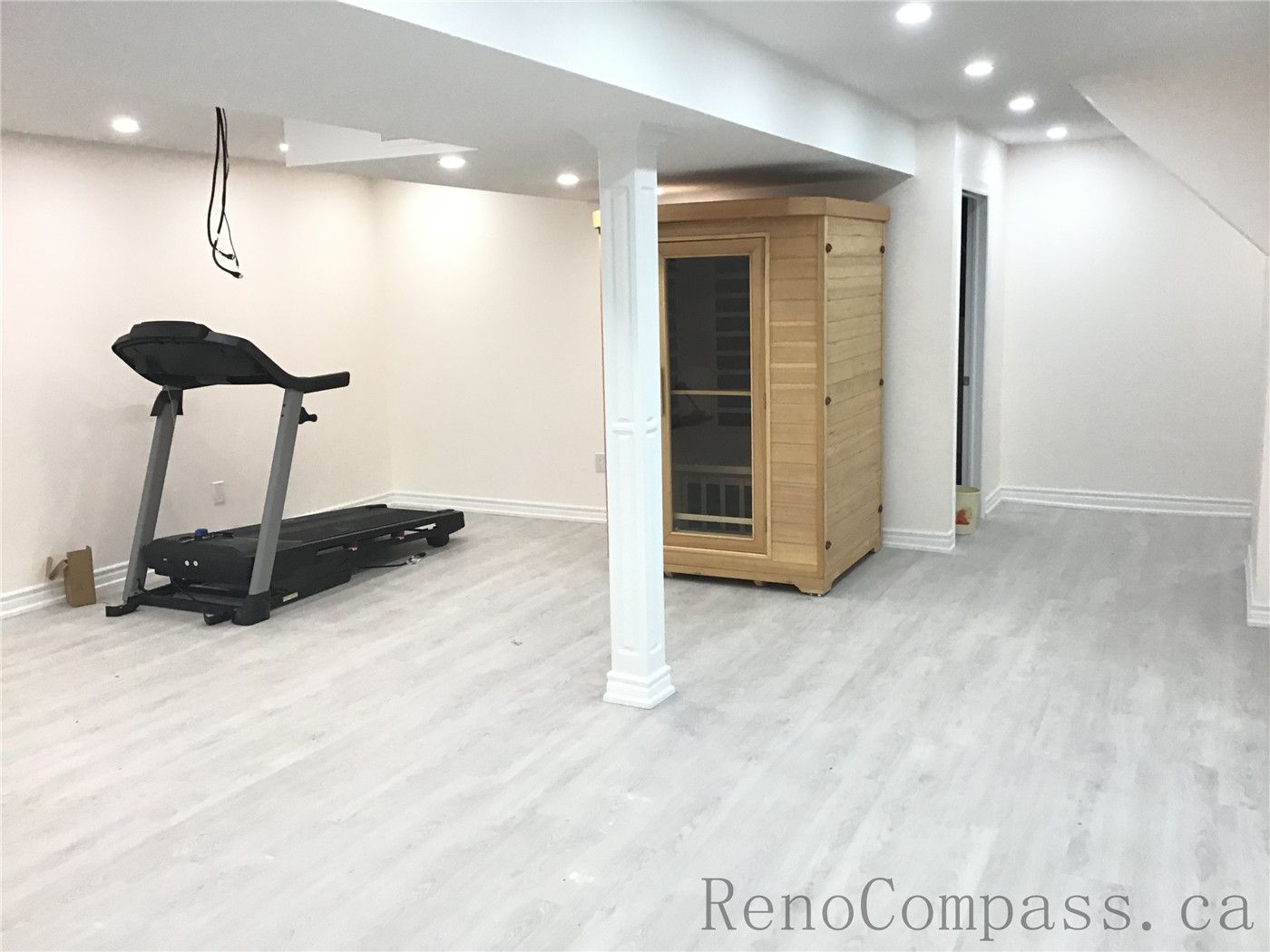 This Pickering basement renovation features a bright and modern finished basement with new light grey flooring, recessed pot lights, and fresh neutral wall paint. The upgraded space includes a home gym area with treadmill and a built-in sauna, creating a functional and relaxing multi-purpose basement. Designed and completed by Reno Compass Inc., a trusted Toronto Renovation Company.