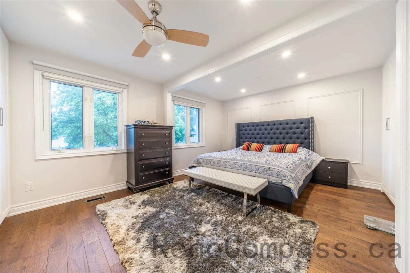 This primary bedroom is part of a North York interior renovation, designed to create a calm and comfortable retreat. The space features warm hardwood flooring, recessed ceiling lights, and a modern ceiling fan for improved airflow. Large windows allow natural light to fill the room, while the upholstered headboard wall adds depth and visual interest. Clean wall detailing, balanced proportions, and a functional layout reflect the quality craftsmanship and thoughtful design typical of professional Toronto interior renovation projects.