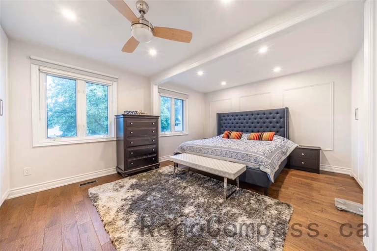 This primary bedroom is part of a North York interior renovation, designed to create a calm and comfortable retreat. The space features warm hardwood flooring, recessed ceiling lights, and a modern ceiling fan for improved airflow. Large windows allow natural light to fill the room, while the upholstered headboard wall adds depth and visual interest. Clean wall detailing, balanced proportions, and a functional layout reflect the quality craftsmanship and thoughtful design typical of professional Toronto interior renovation projects.