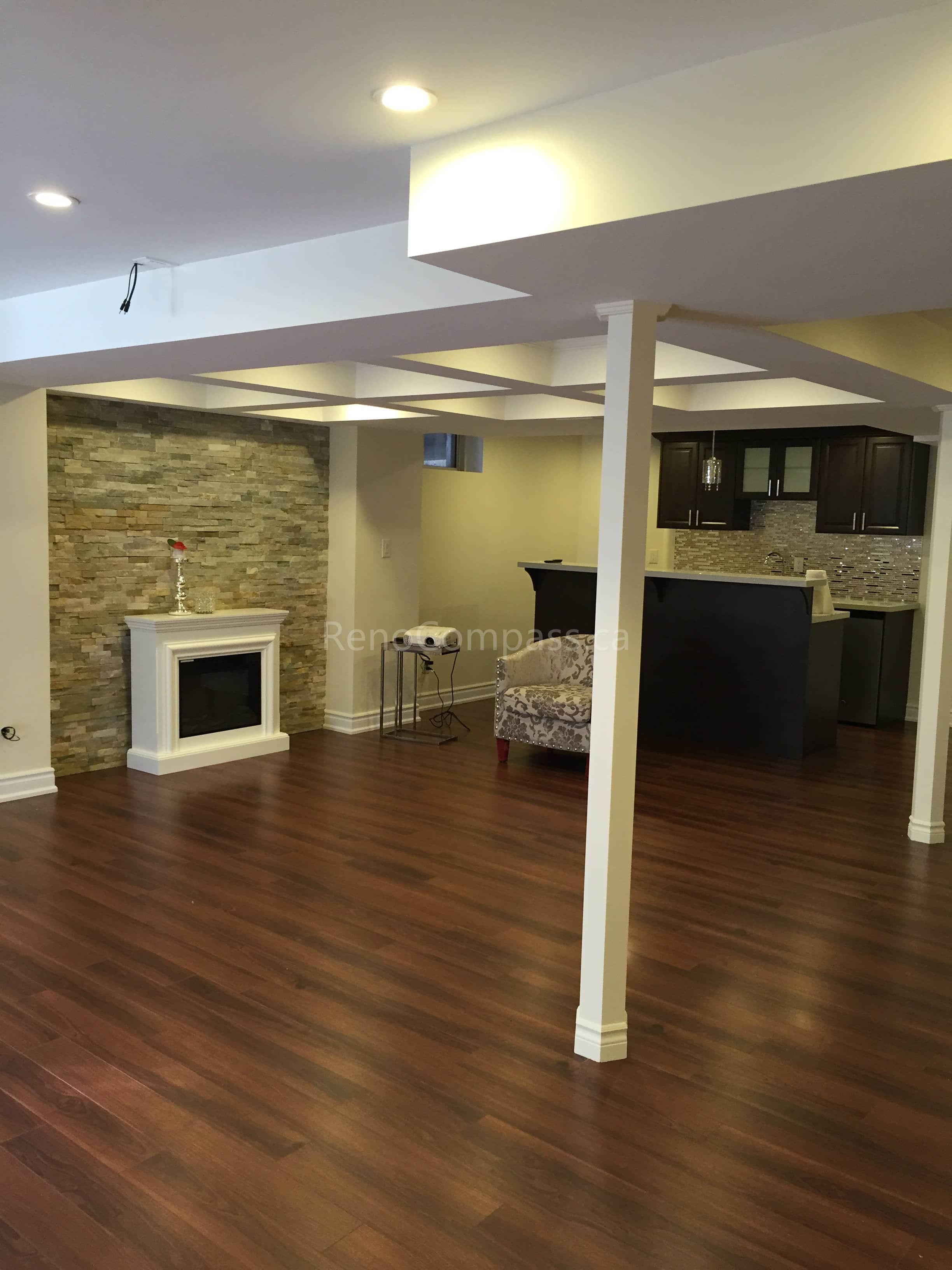 Open-concept basement renovation in Toronto featuring new hardwood flooring, finished support columns, and a modern stone fireplace feature wall. The upgraded layout includes a functional entertainment area and stylish bar space, creating a warm and inviting environment for family gatherings. Completed by Reno Compass, a trusted Toronto renovation company, this project highlights quality craftsmanship and practical basement living design for modern homes.