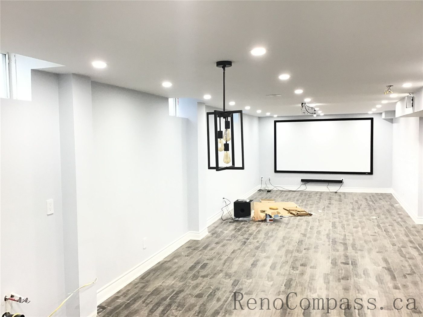 Newly finished basement home theater in Richmond Hill featuring a large wall-mounted projector screen, ceiling-mounted projector setup, recessed pot lights, and durable vinyl plank flooring. This entertainment-focused basement renovation creates a comfortable and modern media space completed by a reliable Toronto Renovation Company.