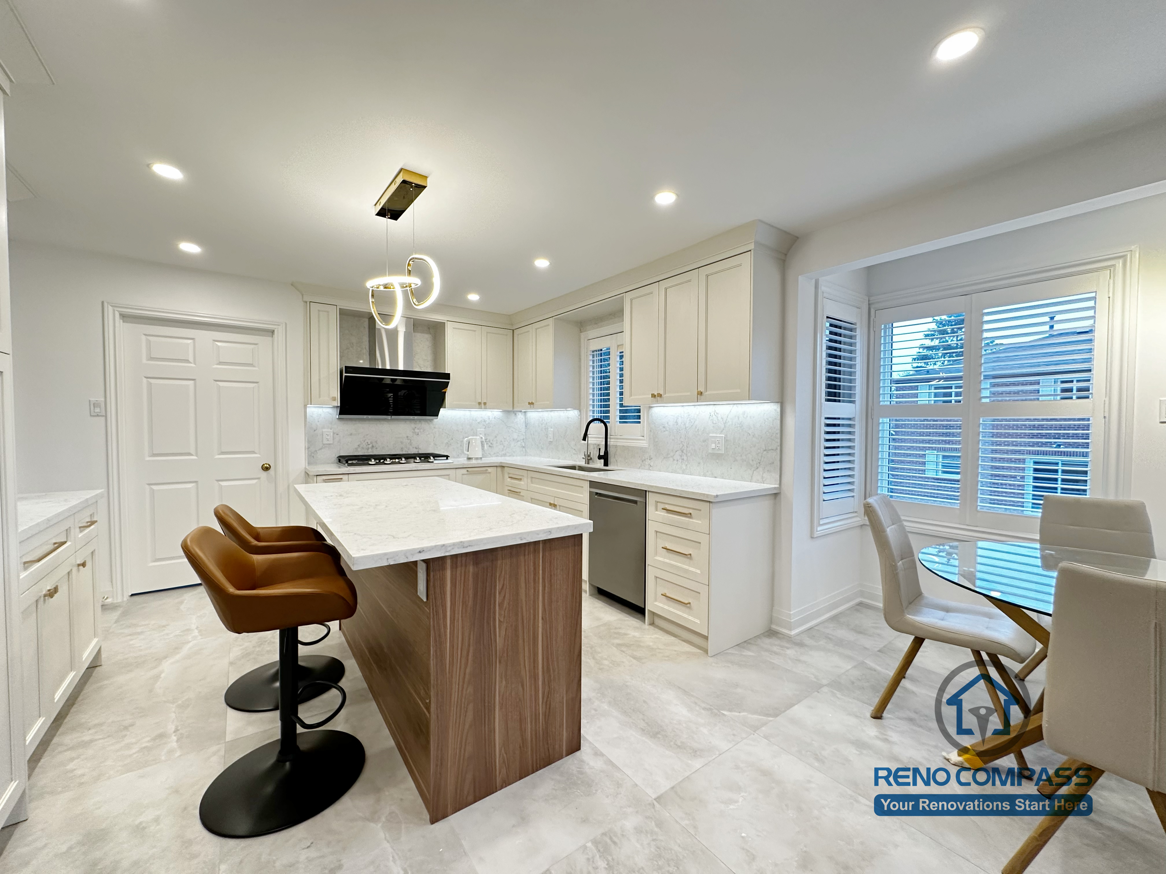 This Markham kitchen renovation showcases a spacious central island with quartz countertop, custom wood base cabinetry, and an open-concept layout that connects seamlessly to the living area. The design balances white perimeter cabinets with warm wood tones, improving both storage capacity and visual depth. Recessed lighting and modern pendant fixtures enhance overall brightness and functionality, making the kitchen ideal for daily cooking and entertaining.