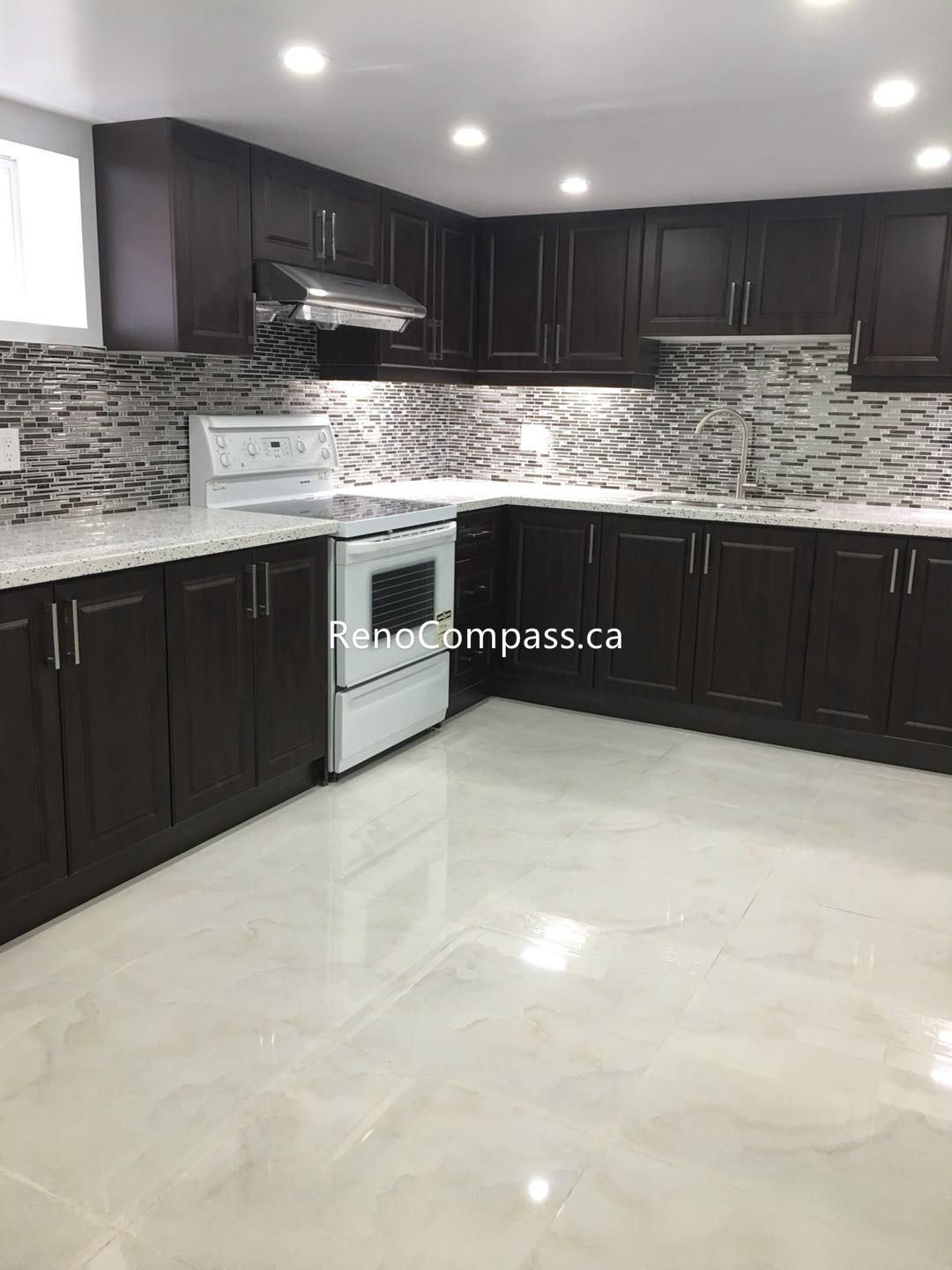 This Toronto basement renovation features a newly built modern kitchen with custom dark wood cabinetry, sleek stone countertops, and a stylish mosaic backsplash. The bright tile flooring and recessed lighting create a clean, spacious, and functional basement living area. Completed by Reno Compass Inc., this basement renovation enhances comfort, usability, and home value with high-quality craftsmanship and contemporary design.