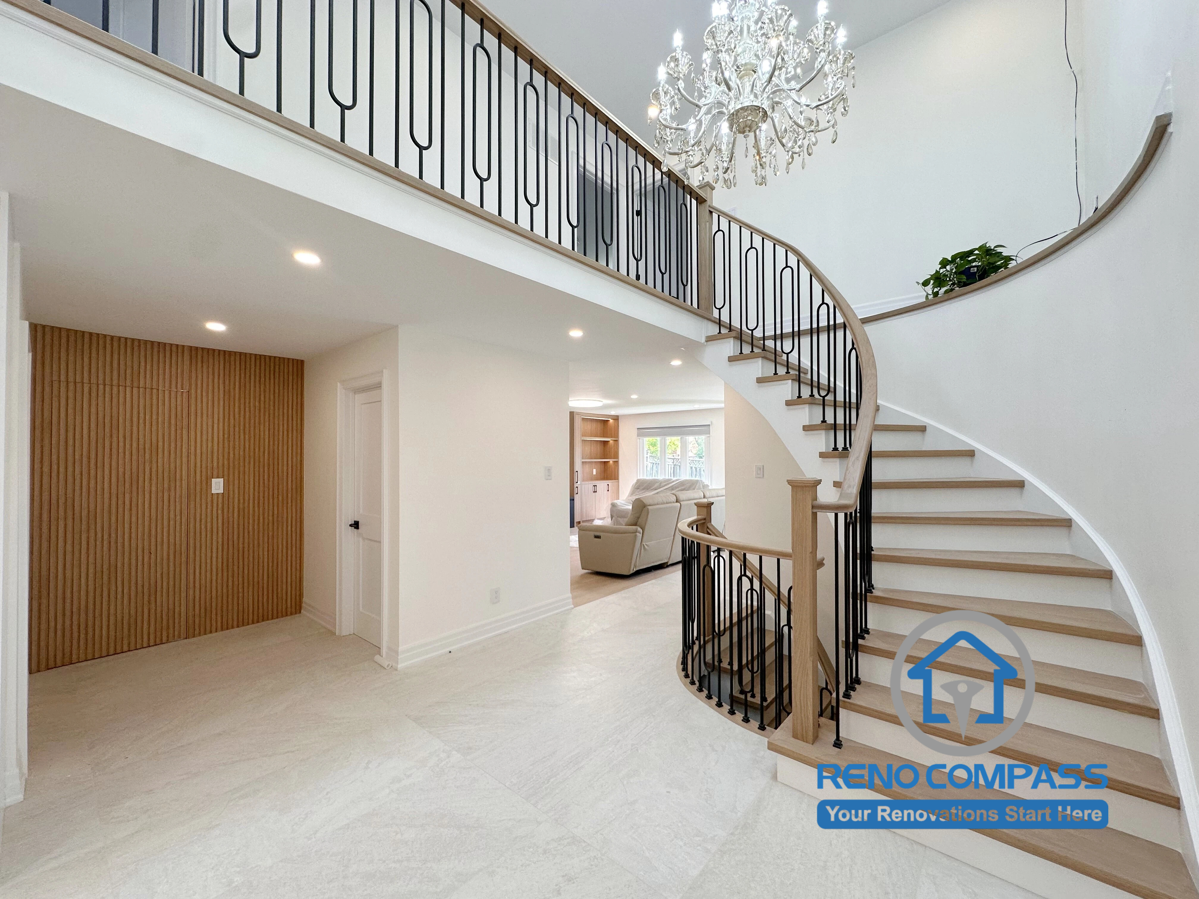 A luxury curved staircase with custom black metal railings, crystal chandelier, wood accents, and an open-concept grand foyer completed by Reno Compass. This whole home renovation project in Markham, Ontario showcases modern interior design, premium craftsmanship, elegant entryway renovation, and custom residential remodeling.