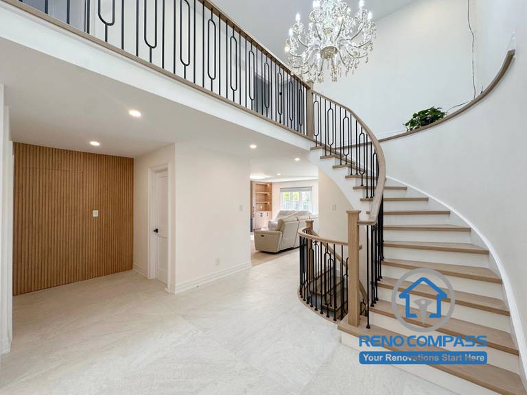 A luxury curved staircase with custom black metal railings, crystal chandelier, wood accents, and an open-concept grand foyer completed by Reno Compass. This whole home renovation project in Markham, Ontario showcases modern interior design, premium craftsmanship, elegant entryway renovation, and custom residential remodeling.