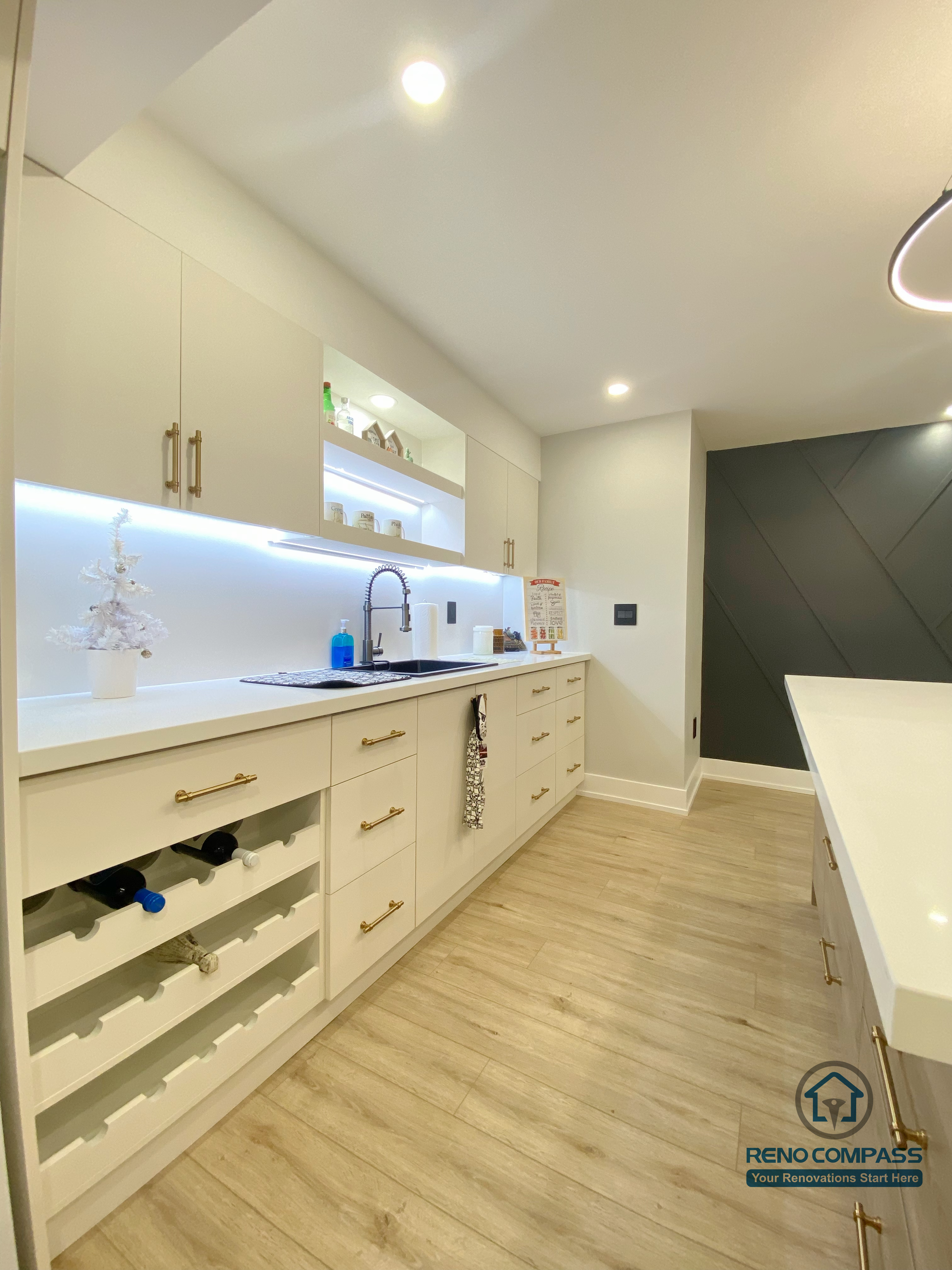 This Aurora basement renovation highlights a modern kitchen area with custom cabinetry, integrated wine storage, under-cabinet LED lighting, and clean minimalist finishes. Light wood flooring and soft neutral tones enhance brightness while maximizing storage and functionality in the basement kitchen layout. Completed by a Toronto renovation company, this project demonstrates practical kitchen design tailored for basement living and entertainment use.
