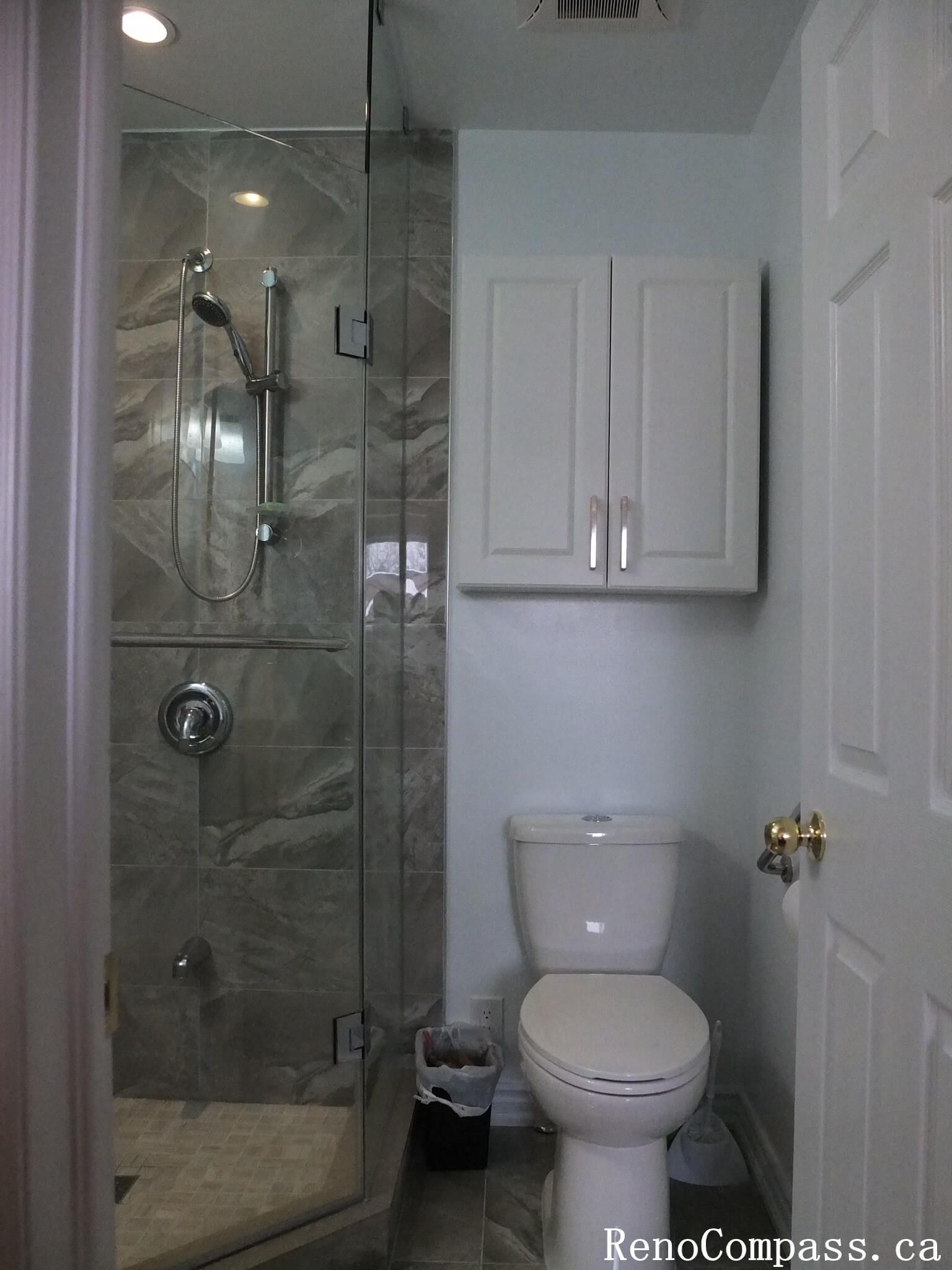 Modern bathroom renovation in North York featuring a glass-enclosed shower, marble-look wall tiles, compact layout design, and clean white cabinetry. This interior renovation focuses on space efficiency, neutral tones, and durable finishes, ideal for small to mid-size Toronto homes.