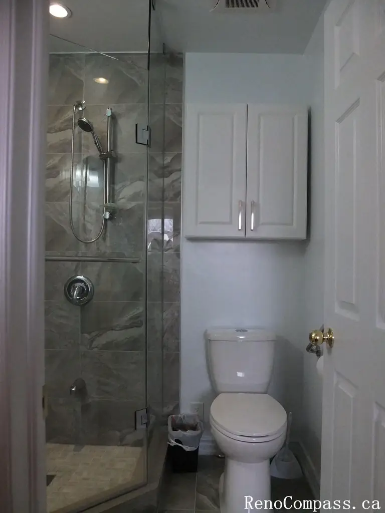 Modern bathroom renovation in North York featuring a glass-enclosed shower, marble-look wall tiles, compact layout design, and clean white cabinetry. This interior renovation focuses on space efficiency, neutral tones, and durable finishes, ideal for small to mid-size Toronto homes.