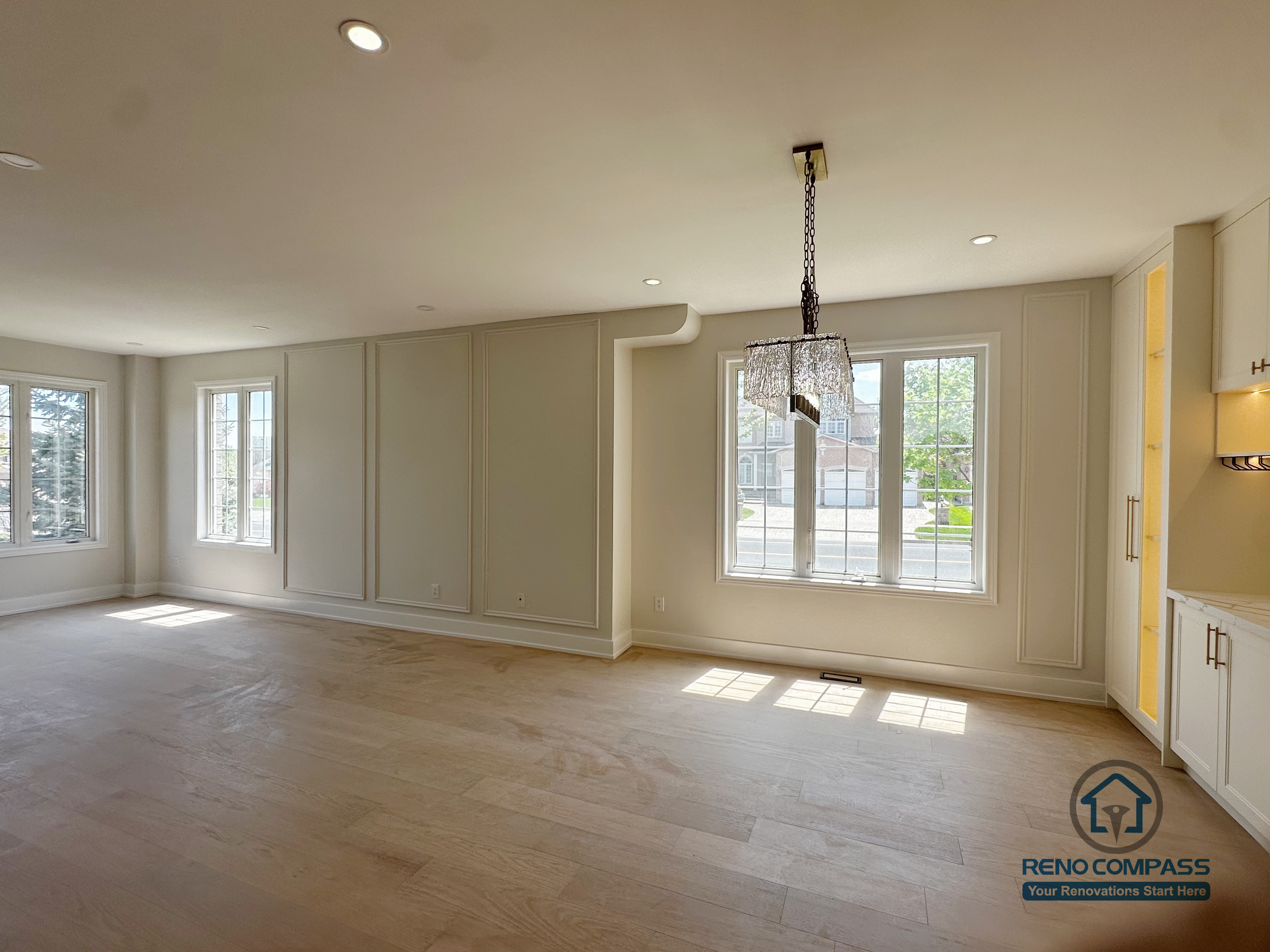 This image highlights the open living and dining area from a Markham interior renovation, designed to maximize natural light and spatial openness. Large windows along the exterior wall bring in abundant daylight, enhancing the warmth of the light wood flooring and creating a bright, welcoming atmosphere throughout the space.

The wall panel detailing adds subtle architectural rhythm without overwhelming the room, while recessed ceiling lights and a statement chandelier define the dining zone with a sense of balance and elegance. Clean lines and neutral tones allow the space to remain flexible for different furniture layouts and daily living needs.

By carefully balancing openness, proportion, and lighting, this renovation delivers a refined yet comfortable main-floor living environment. The result reflects Reno Compass’s approach to interior renovation—creating spaces that feel cohesive, functional, and timeless for Markham homes.