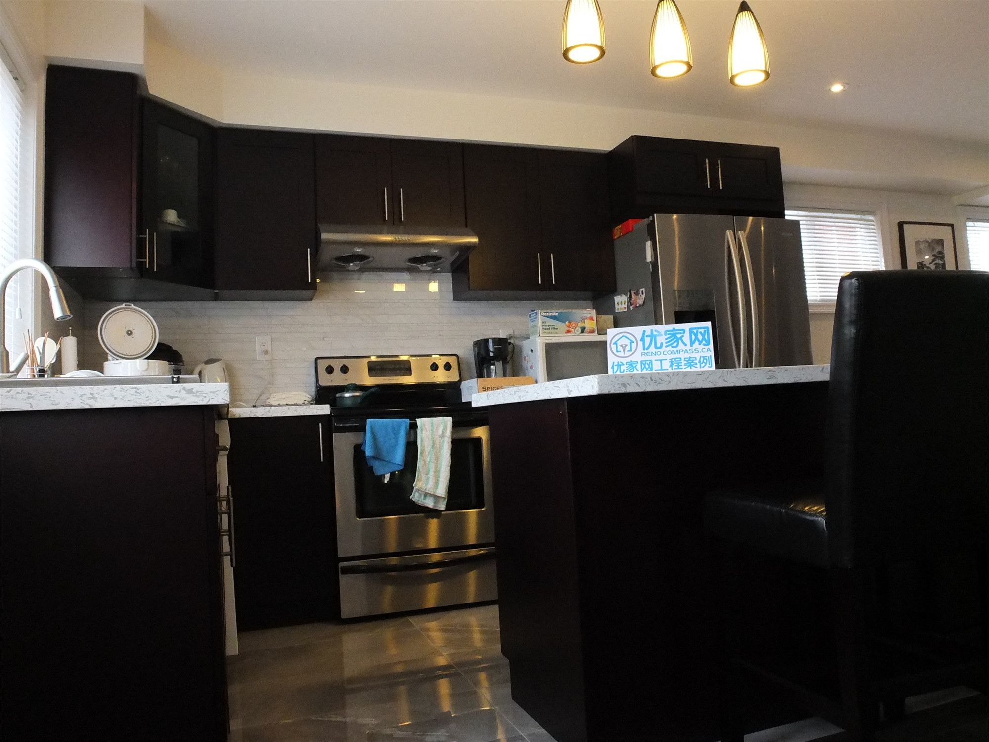 Contemporary kitchen from a Scarborough home addition project featuring dark wood cabinetry, quartz countertops, stainless steel appliances, and a functional kitchen island with pendant lighting. The renovation enhances both cooking efficiency and modern interior aesthetics within the expanded living space.