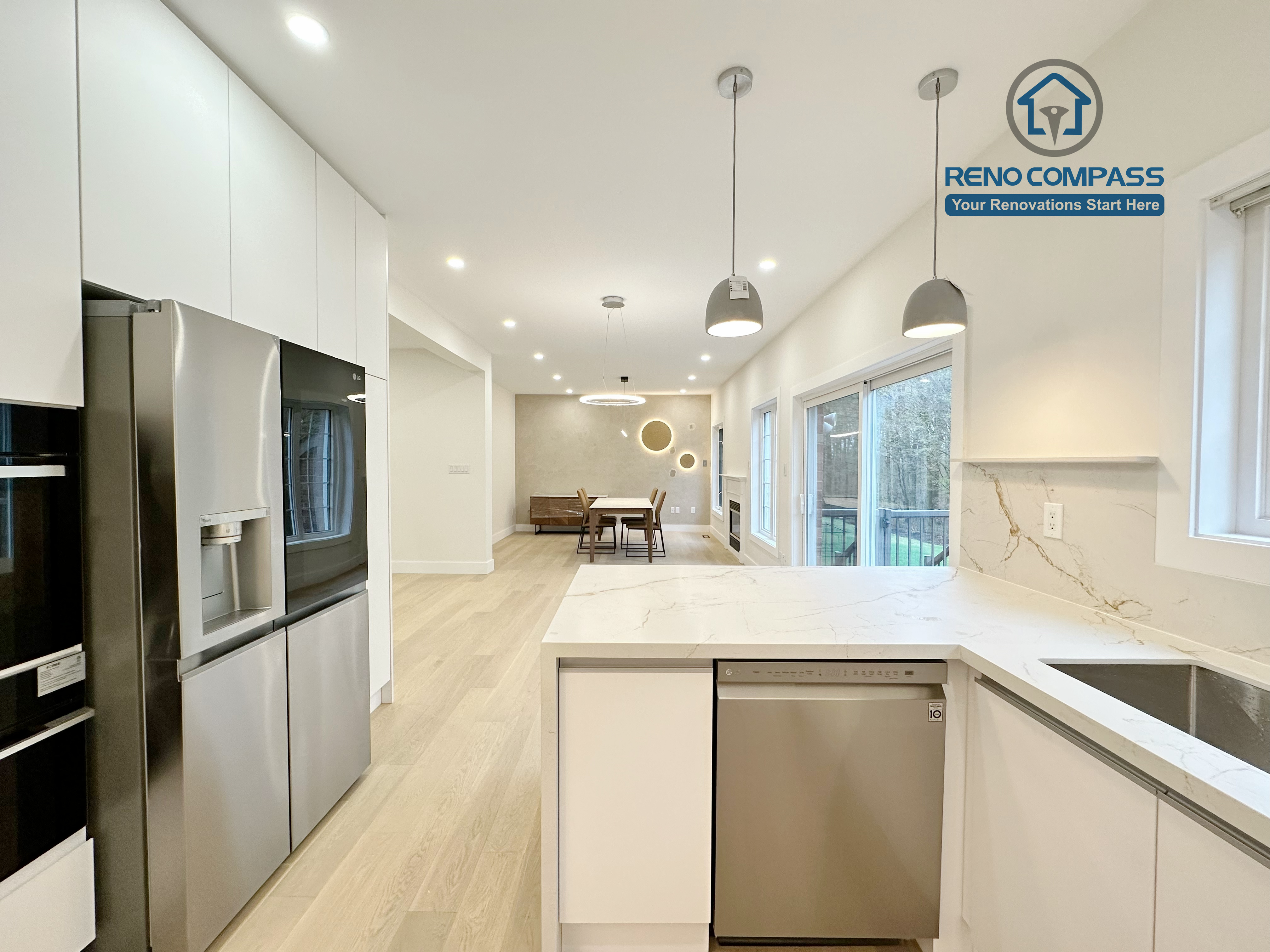 This image highlights a bright open-concept kitchen renovation in Richmond Hill, featuring full-height custom white cabinetry, built-in stainless steel refrigerator and oven, and a large quartz kitchen island with integrated dishwasher and sink. Pendant lighting above the island, recessed ceiling lights, and expansive windows bring natural light throughout the space, seamlessly connecting the kitchen to the dining area. Completed by an experienced Toronto Renovation Company, this kitchen renovation focuses on clean lines, modern functionality, and a spacious layout ideal for everyday living and entertaining.
