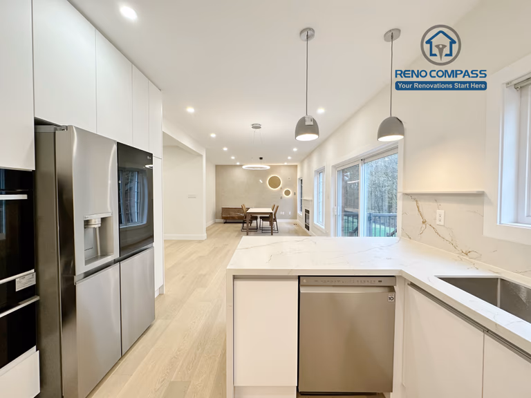 This image highlights a bright open-concept kitchen renovation in Richmond Hill, featuring full-height custom white cabinetry, built-in stainless steel refrigerator and oven, and a large quartz kitchen island with integrated dishwasher and sink. Pendant lighting above the island, recessed ceiling lights, and expansive windows bring natural light throughout the space, seamlessly connecting the kitchen to the dining area. Completed by an experienced Toronto Renovation Company, this kitchen renovation focuses on clean lines, modern functionality, and a spacious layout ideal for everyday living and entertaining.