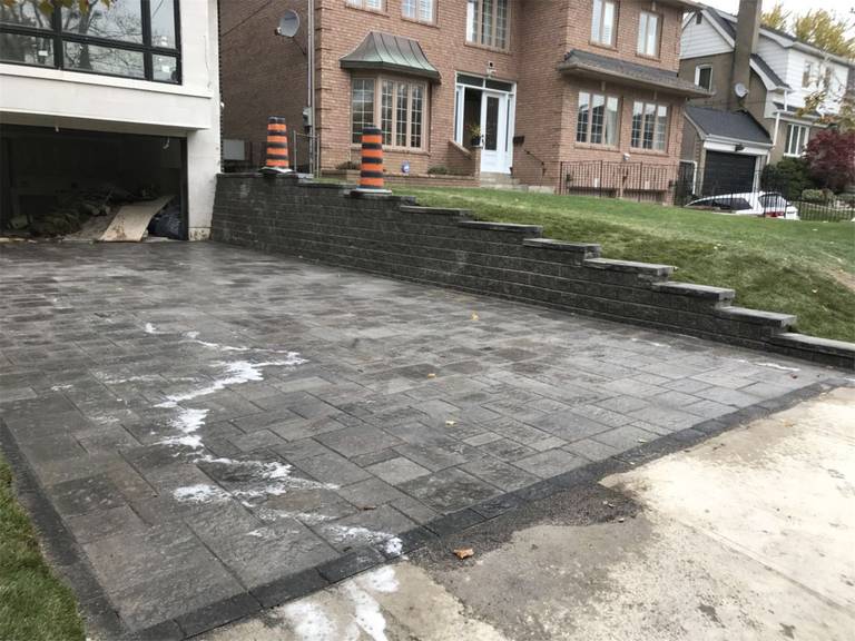 This Markham landscaping renovation features a newly installed interlocking stone driveway combined with a durable retaining wall that supports the elevated lawn area. The structured stone layout provides a clean and modern look while improving driveway stability and drainage. Completed by a trusted Toronto Renovation Company, the project enhances both curb appeal and long-term outdoor functionality.