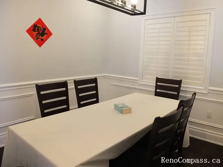 This Newmarket interior renovation features a clean and elegant dining room designed with classic wall wainscoting and rich dark hardwood flooring. Plantation shutters allow natural light to brighten the space while maintaining privacy, and the modern rectangular pendant light provides balanced illumination above the dining table. The simple layout and refined finishes create a comfortable setting for family meals and gatherings. Completed by Reno Compass Inc., this project highlights timeless interior design and high-quality craftsmanship for modern homes.